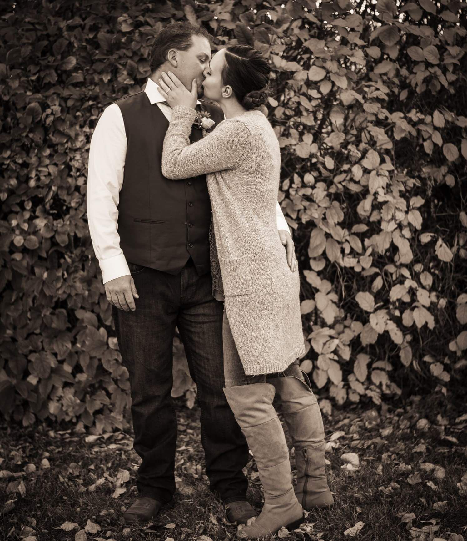 A romantic vintage-style portrait of a couple embracing against a leafy backdrop.
