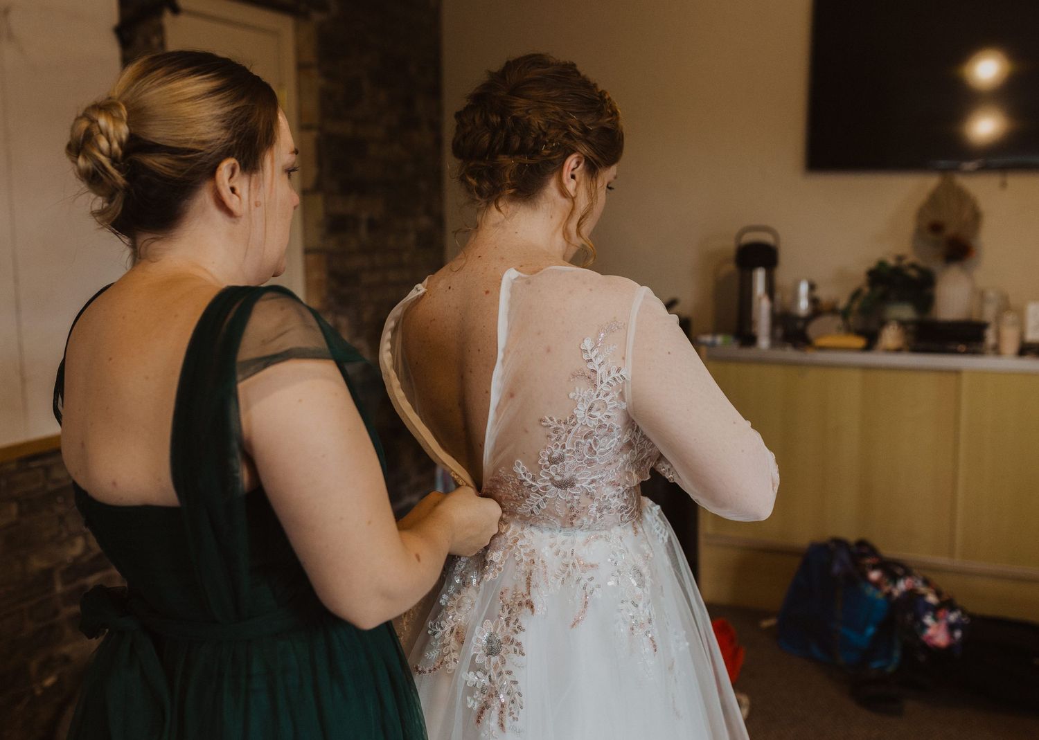 Wedding dress preparation with emerald green bridesmaid dresses visible in the background.