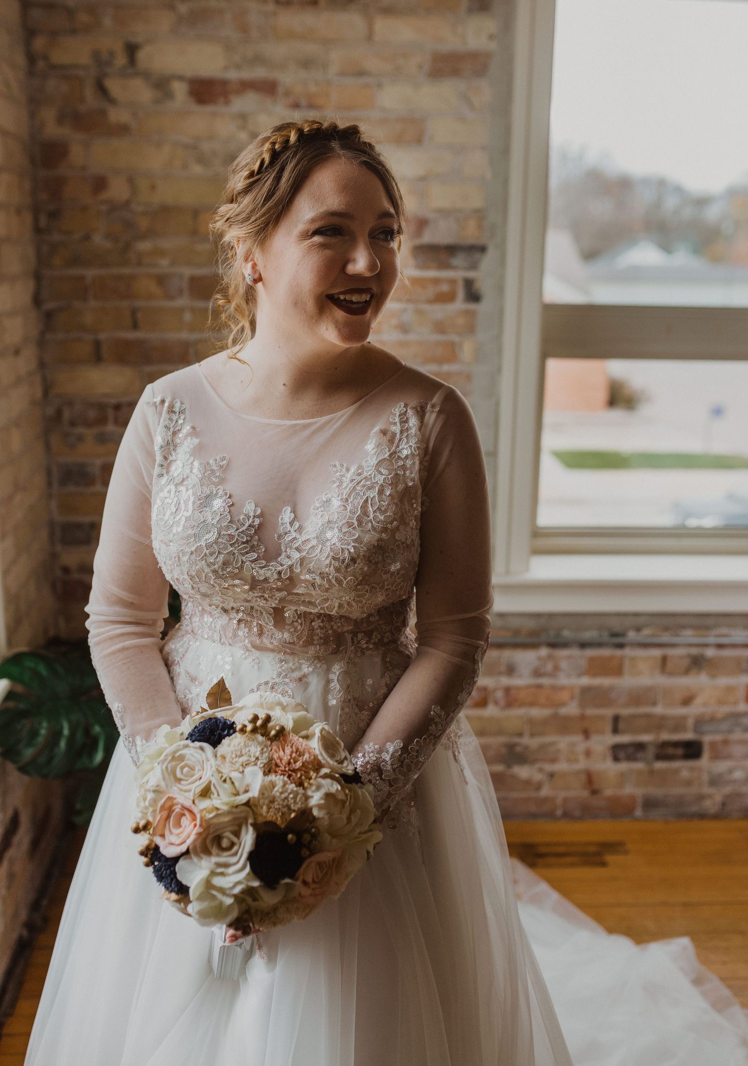 A bride in a lace-detailed wedding dress holds a romantic bouquet of mixed flowers.