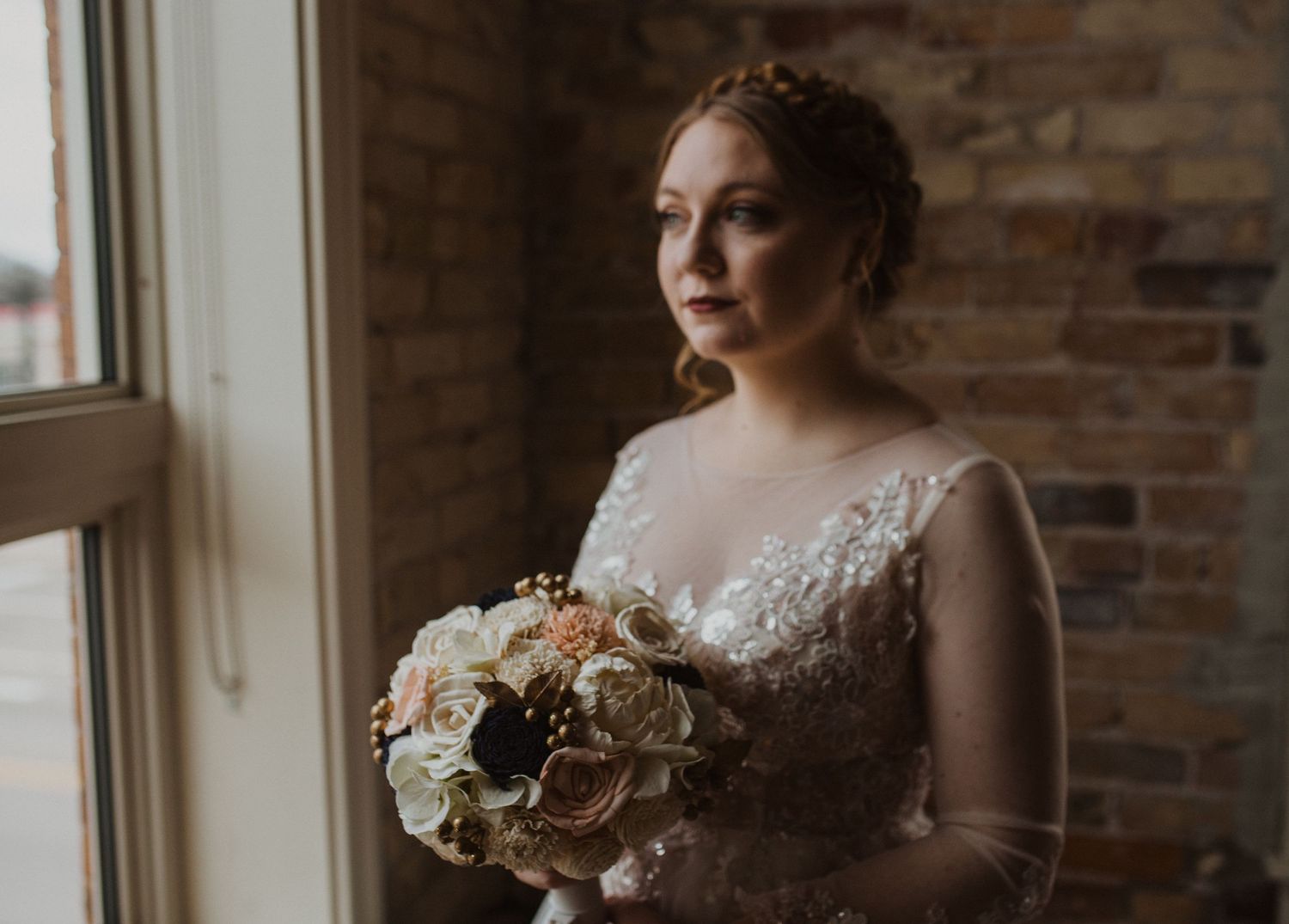 Elegant bridal portrait in front of exposed brick wall with natural window light.