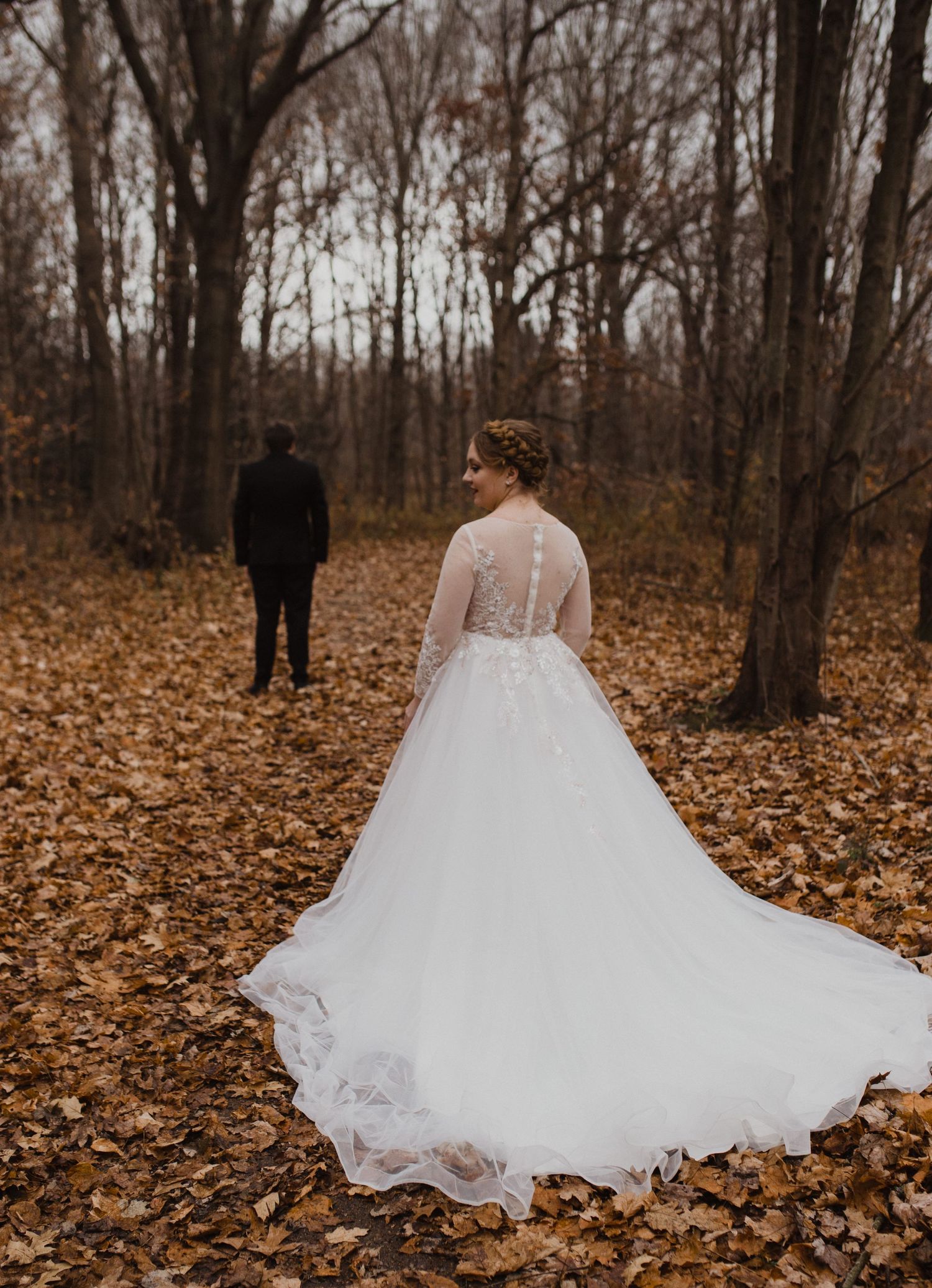 White wedding dress with flowing train spread across autumn leaves in a forest setting.