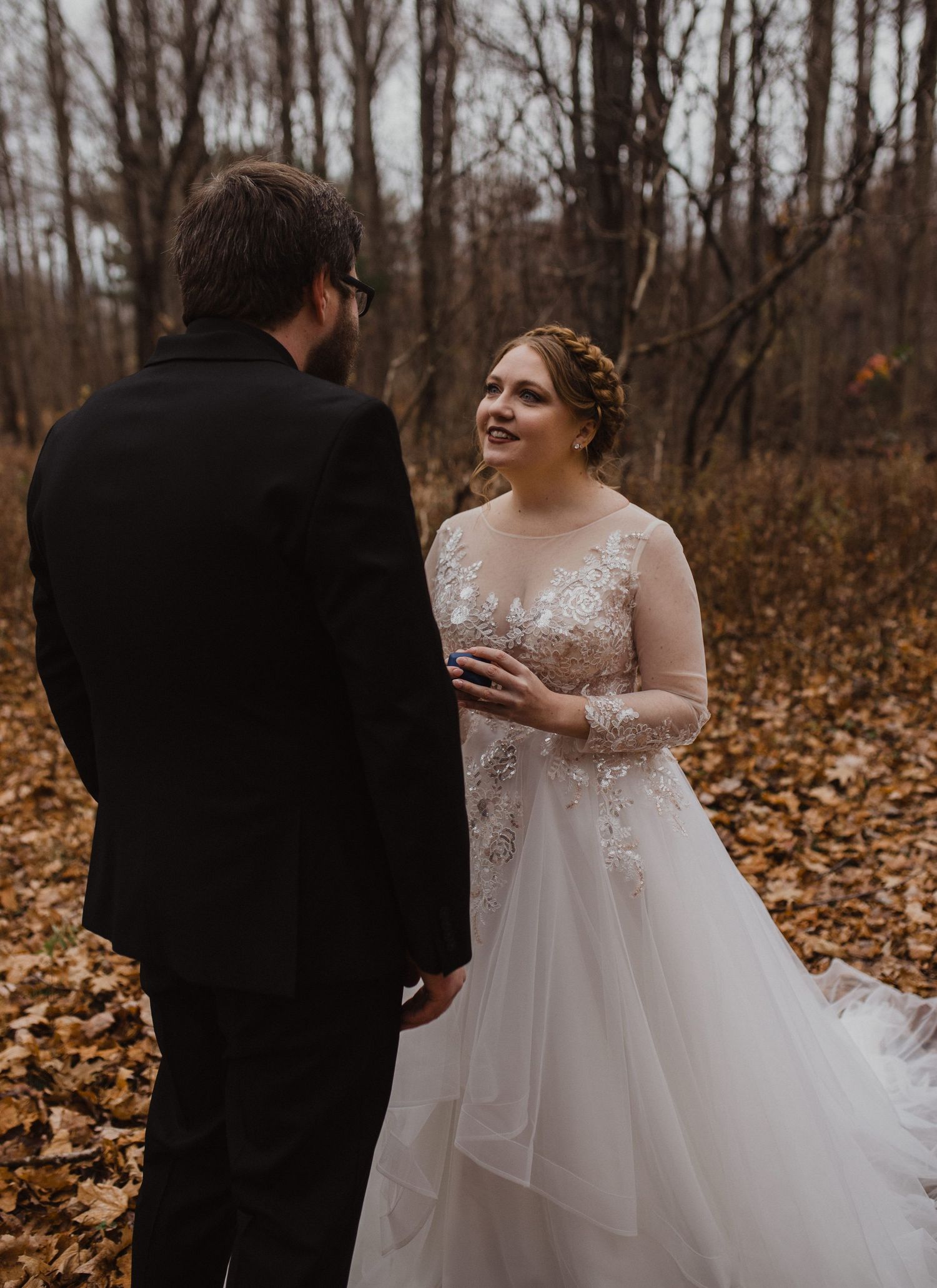 Wedding vow exchange captured in wooded setting with fall leaves.