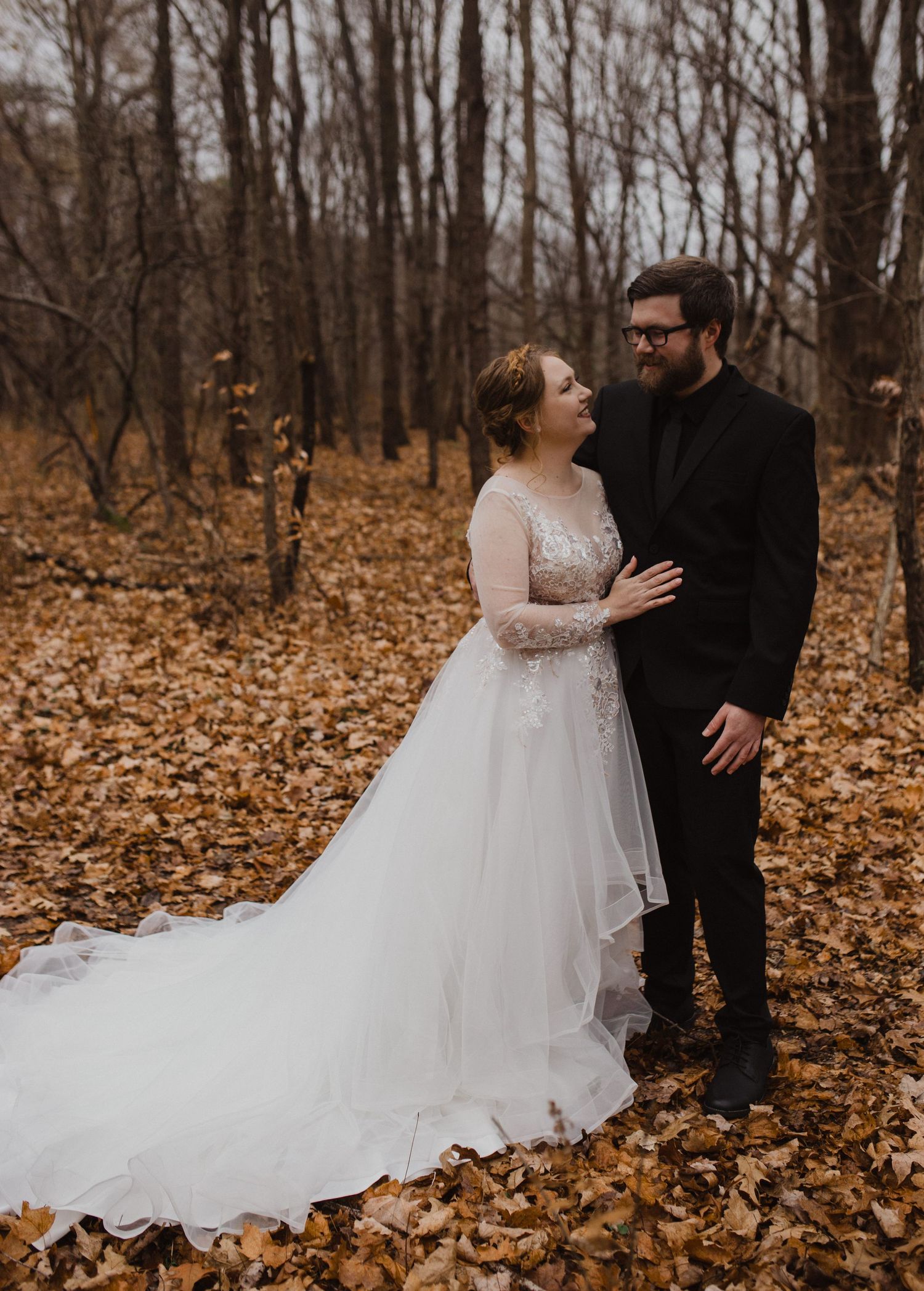 Romantic wedding portrait on forest floor covered in autumn leaves.