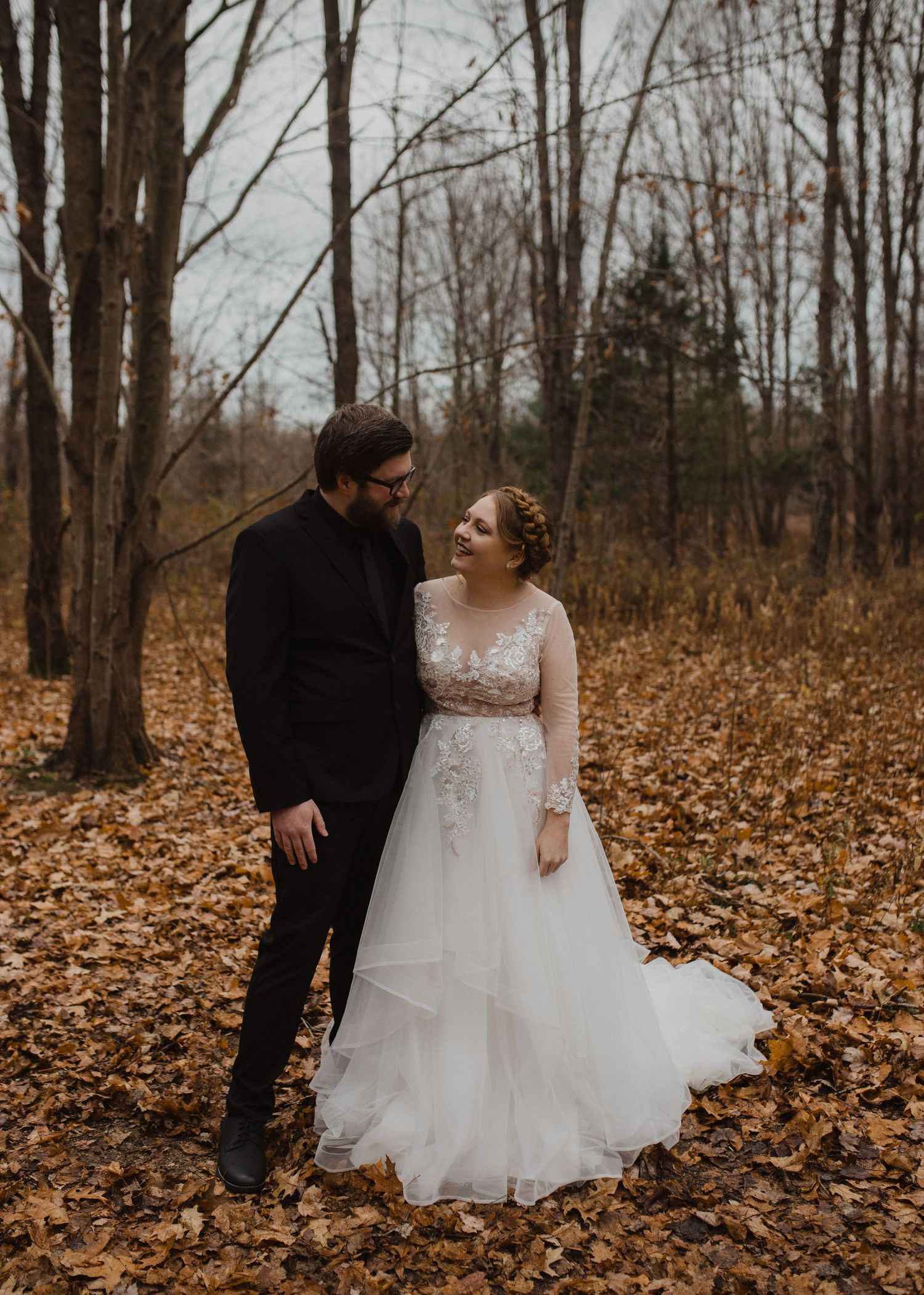 A couple laughs together during their wedding photoshoot in a fall forest setting.