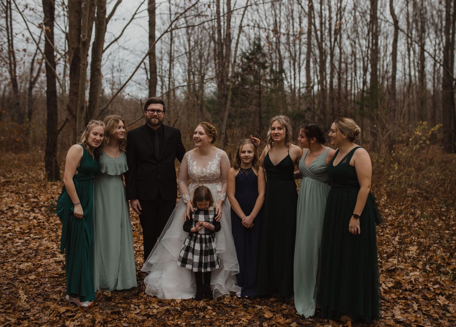 Wedding party in mixed formal attire poses together among autumn trees.