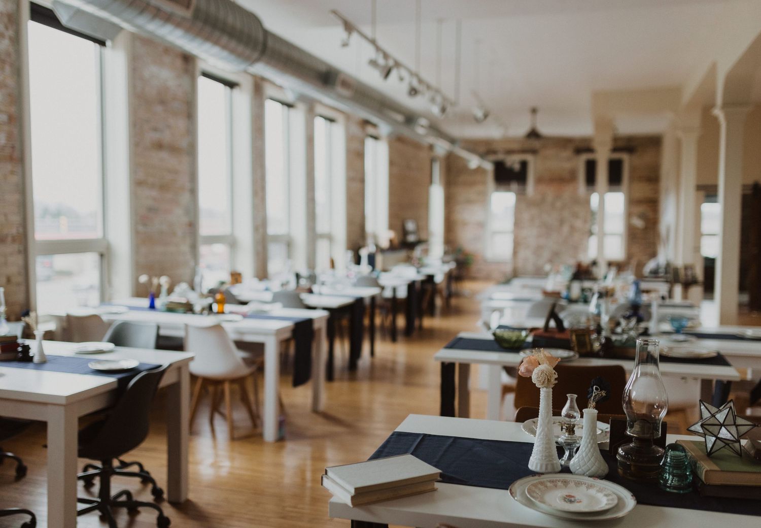 Long dining room with exposed brick walls and elegant table settings for an event.