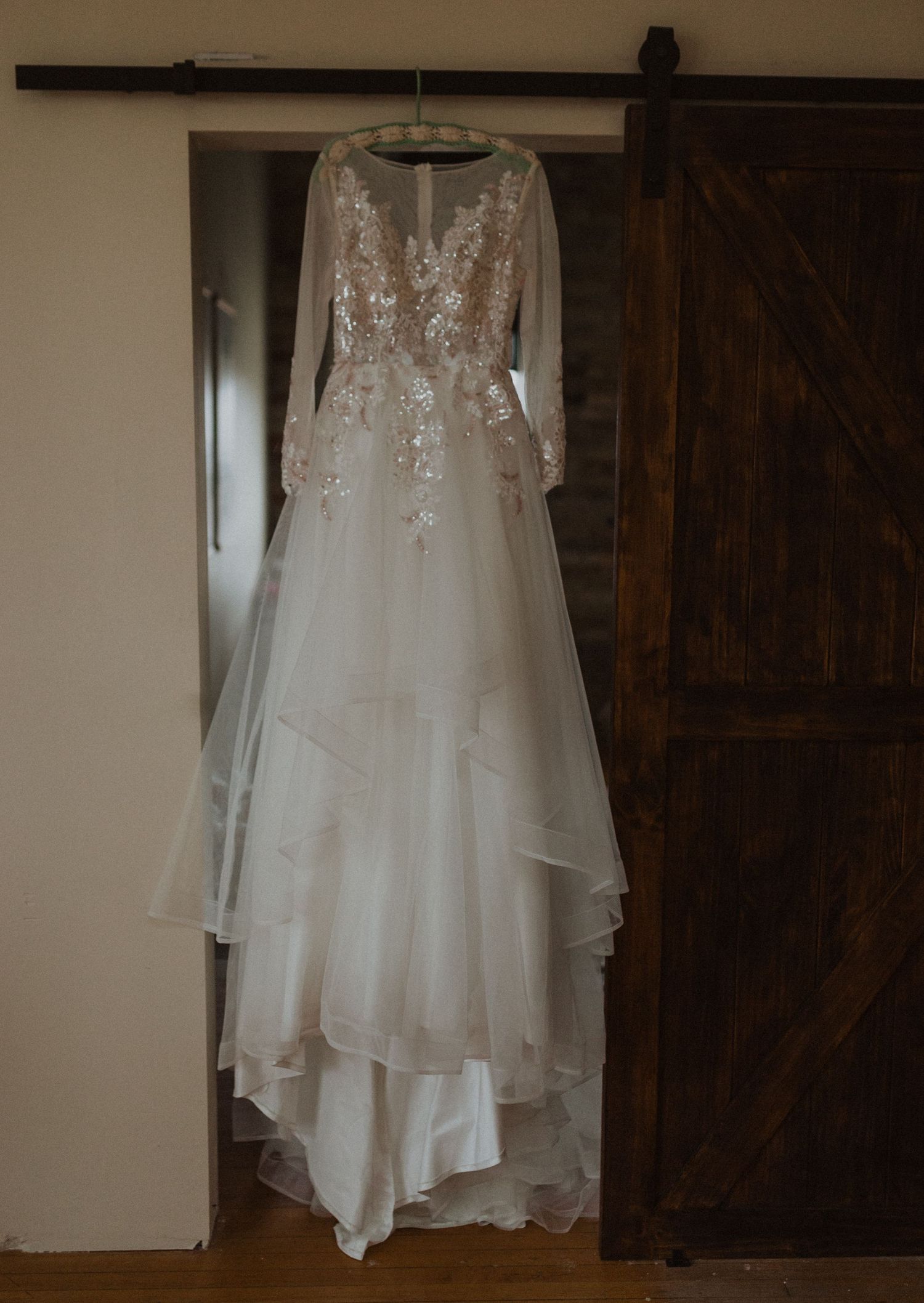 Elegant white lace wedding dress with long sleeves hanging against a rustic barn door.