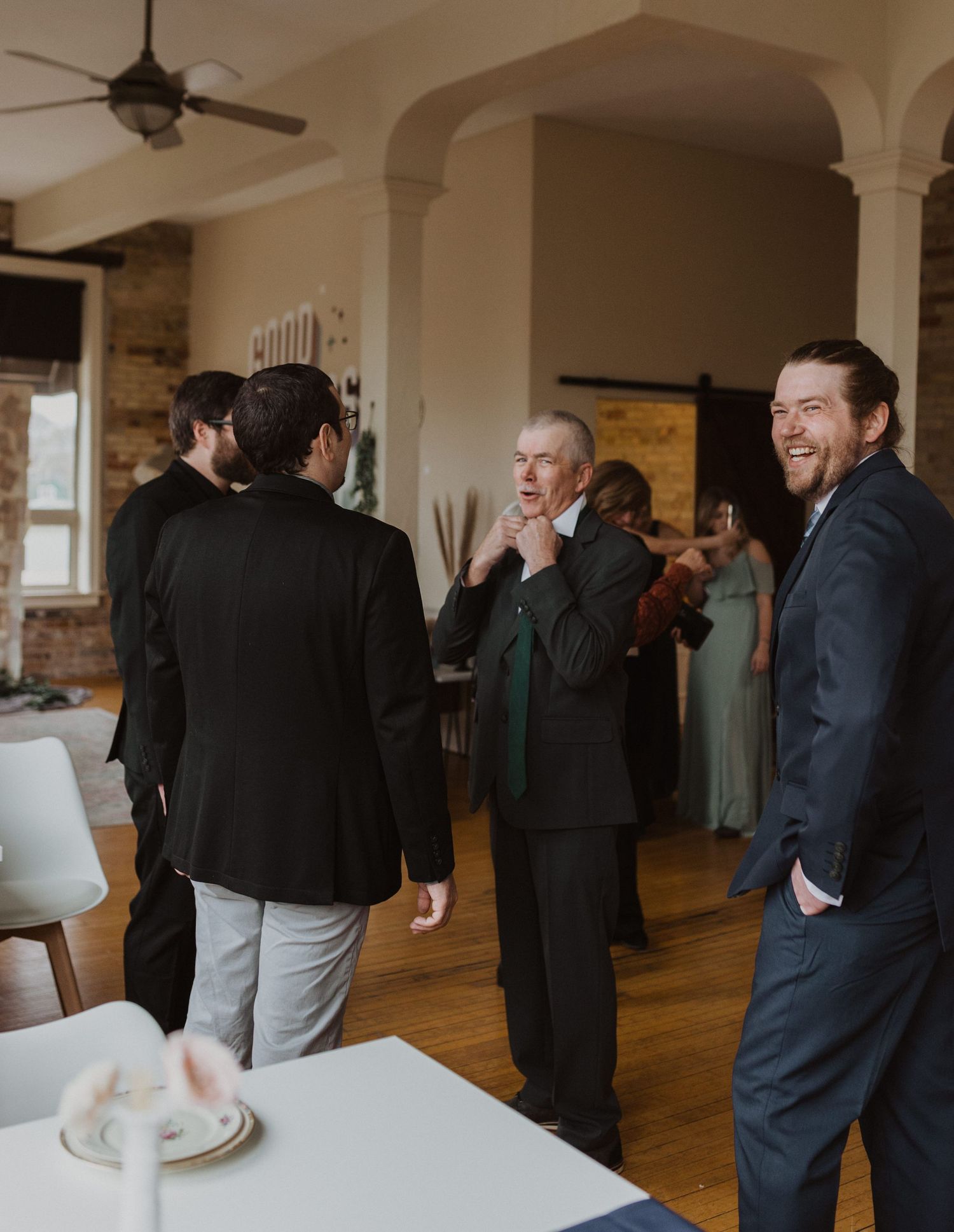 Wedding guests mingling in a spacious room with white columns and exposed brick walls.