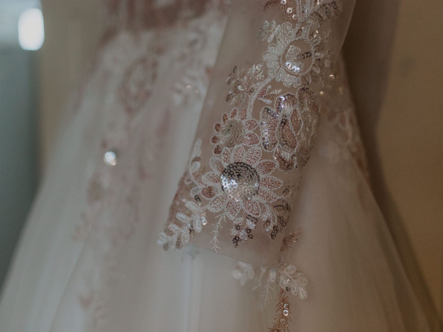 Close-up detail of intricate lace and beadwork on a white wedding dress.