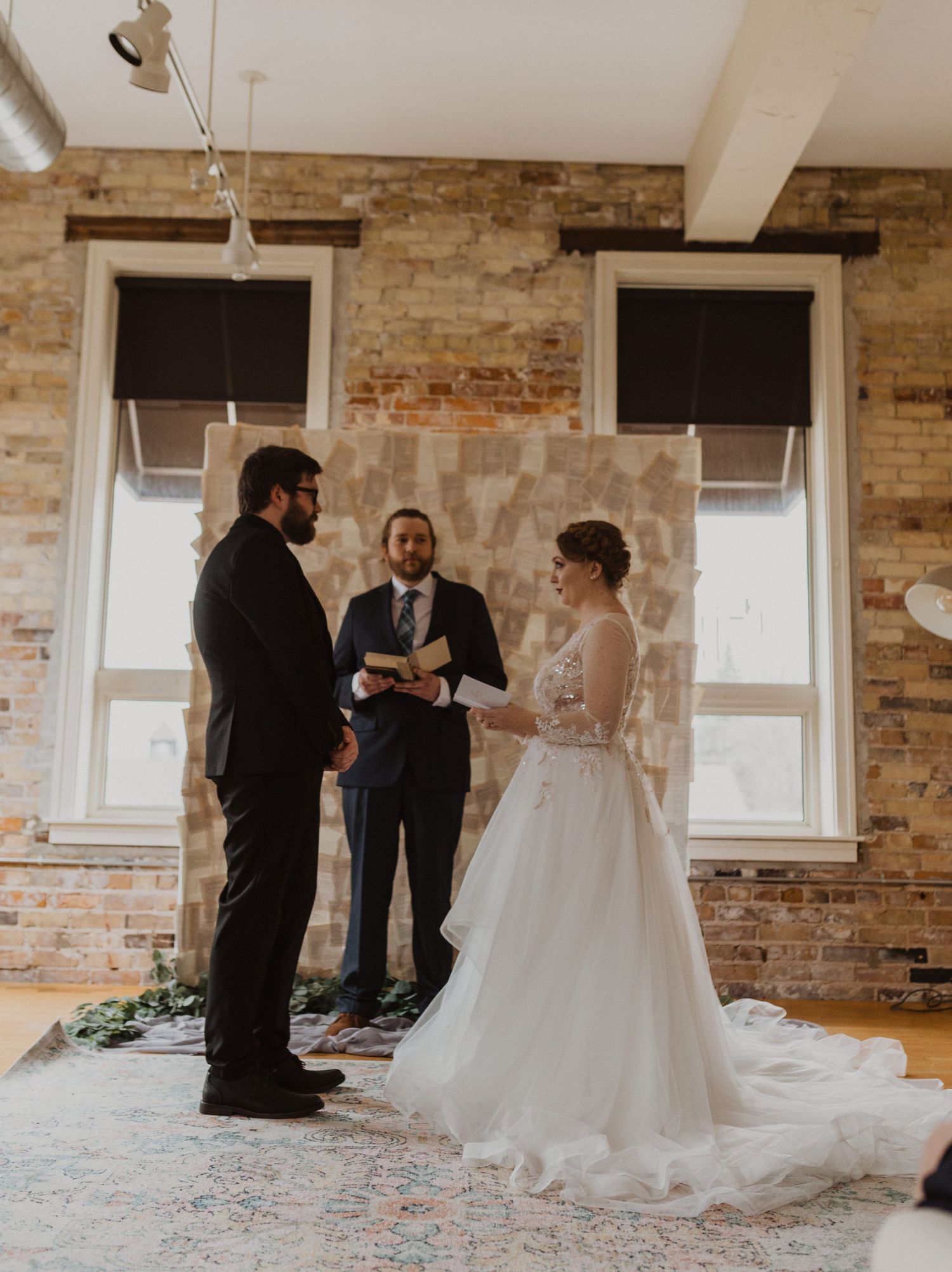 Intimate wedding ceremony moment in a rustic brick-walled venue with natural window light.