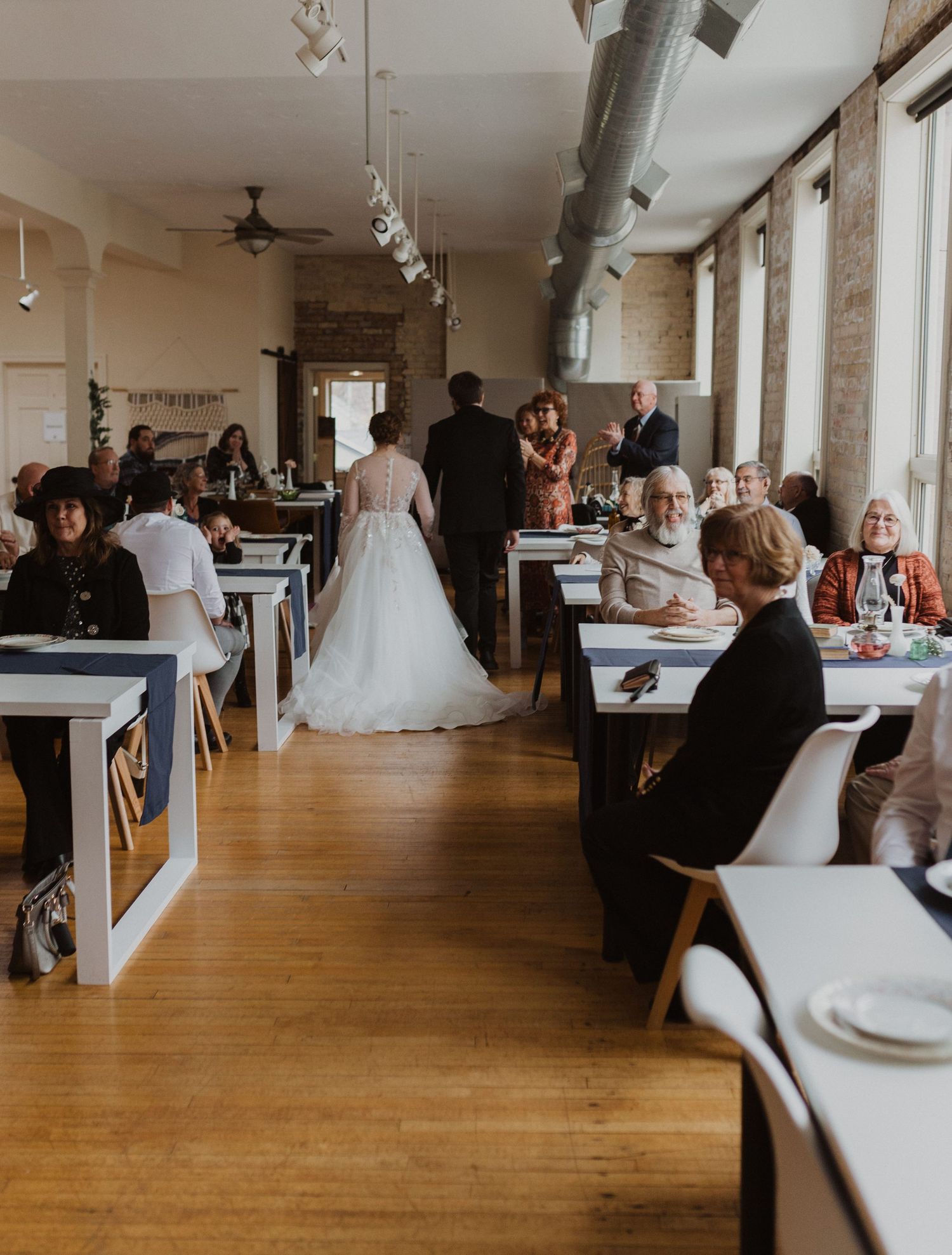 Wedding guests mingle in an elegant venue with hardwood floors and exposed brick walls.