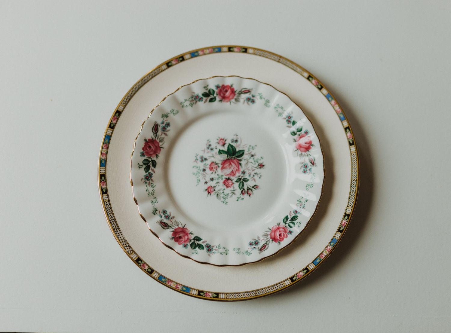 Vintage floral china plate with pink roses and gold trim on gray background.