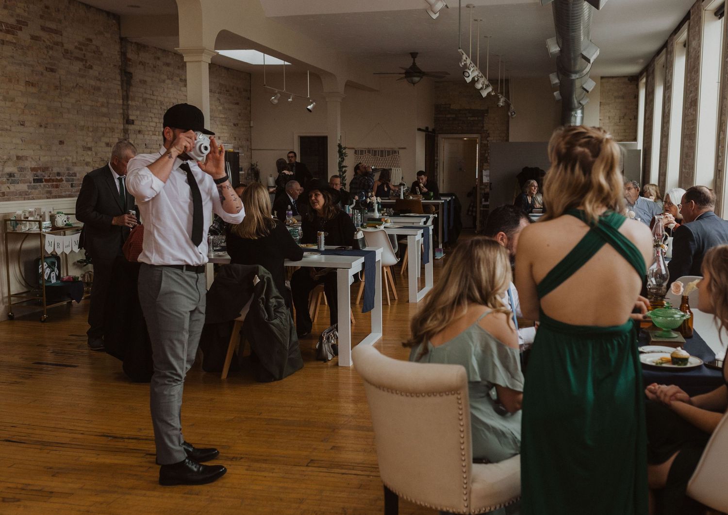 Wedding party gathers in a rustic brick-walled venue with hardwood floors.