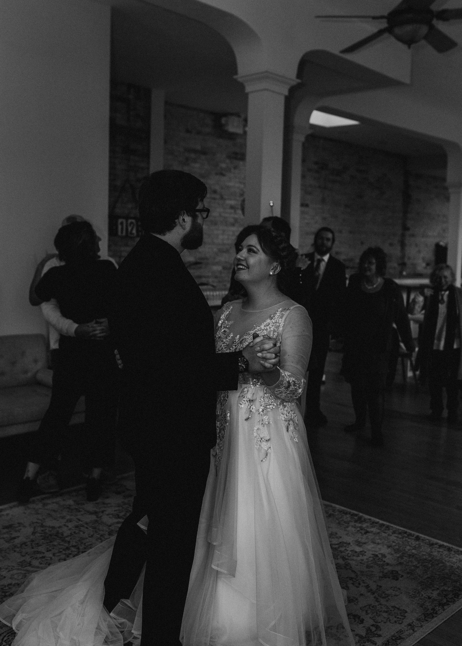 Black and white wedding scene in a spacious venue with exposed brick and ceiling fans.