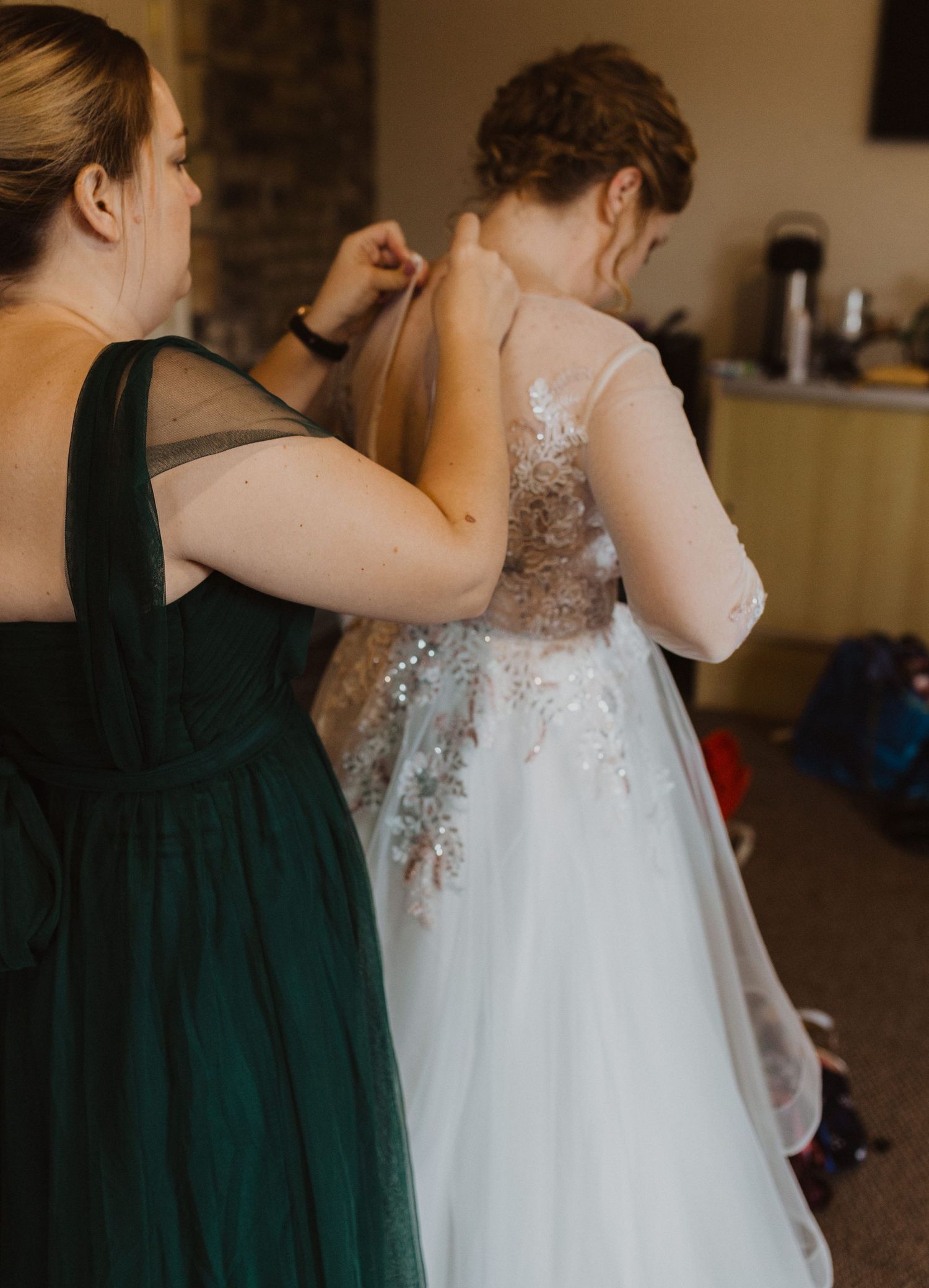 A bride in a lace white wedding gown gets help with final dress adjustments.