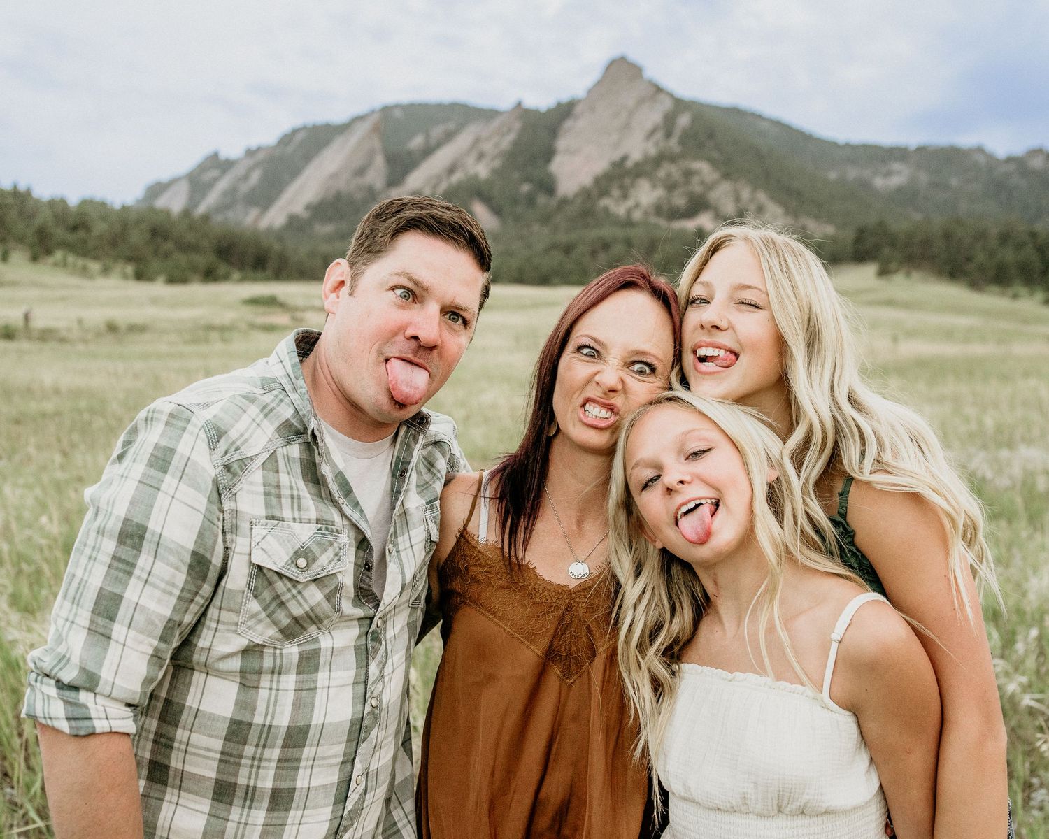 Happy family posing together outdoors with scenic Flatirons rock formations in Boulder, Colorado in background.