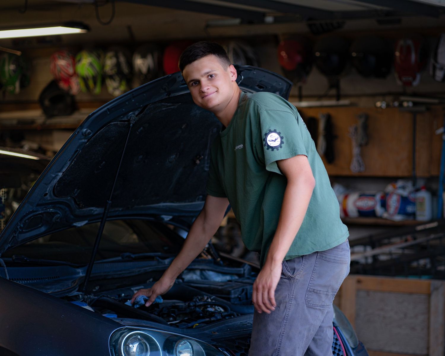 A person wearing a green shirt works on a car engine in a garage workshop.