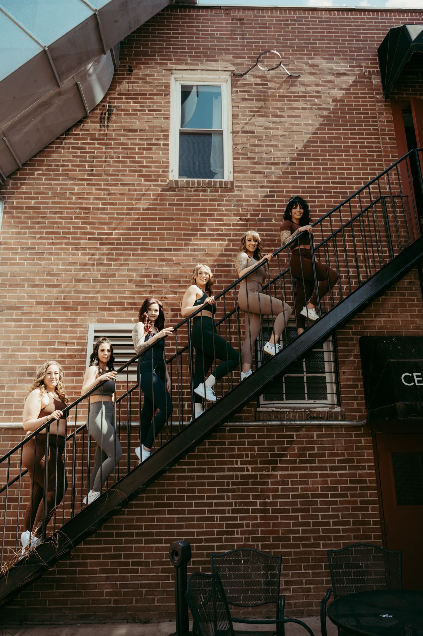 Group poses on exterior brick building staircase in stylish outfits.