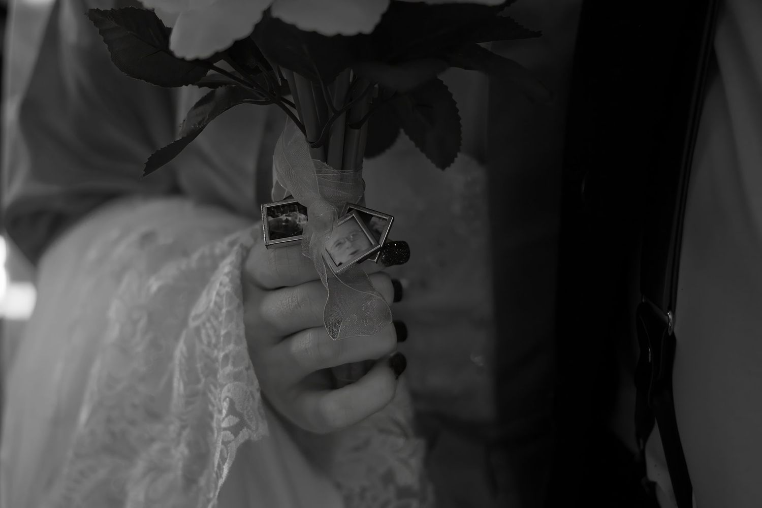 Black and white detail shot of hands holding flowers against lace fabric.