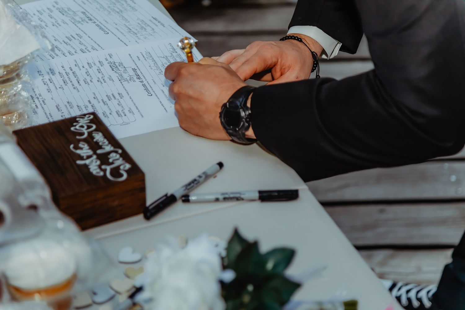 Close up of hands writing on paper at a wedding signing table.