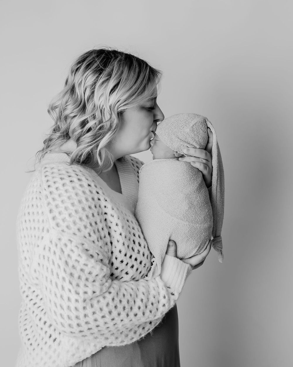 A tender moment captured in black and white as a woman kisses a swaddled baby.