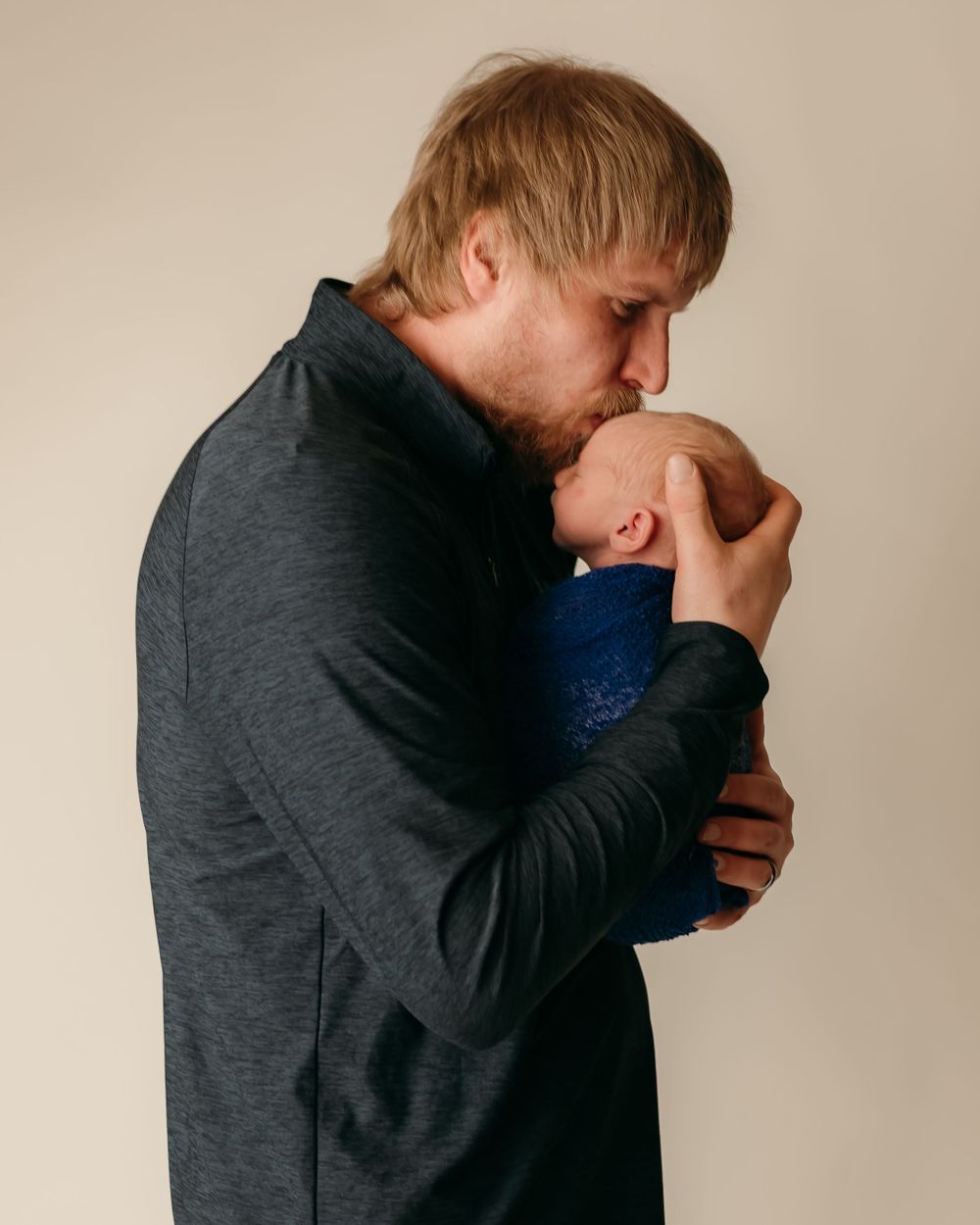 An intimate moment between parent and newborn as they share a gentle kiss while wearing dark clothing.