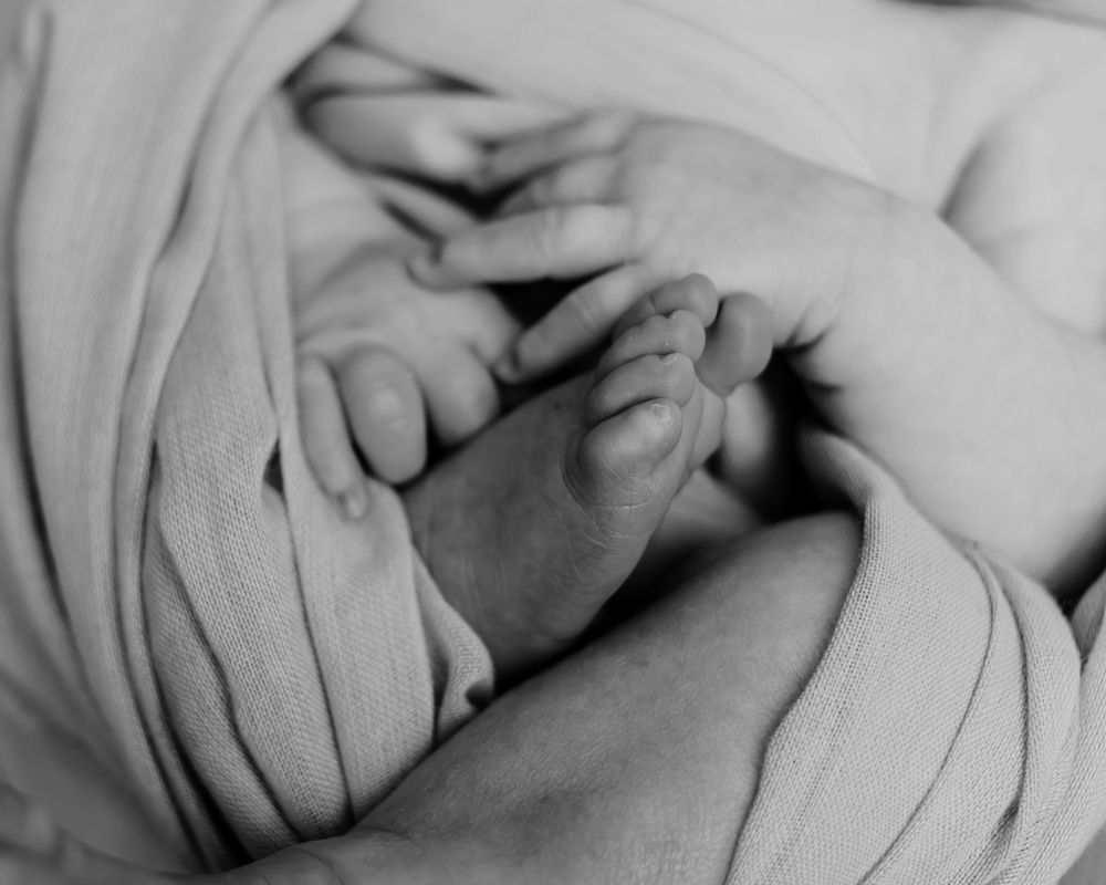 Close-up black and white photo of tiny baby feet wrapped in soft fabric.
