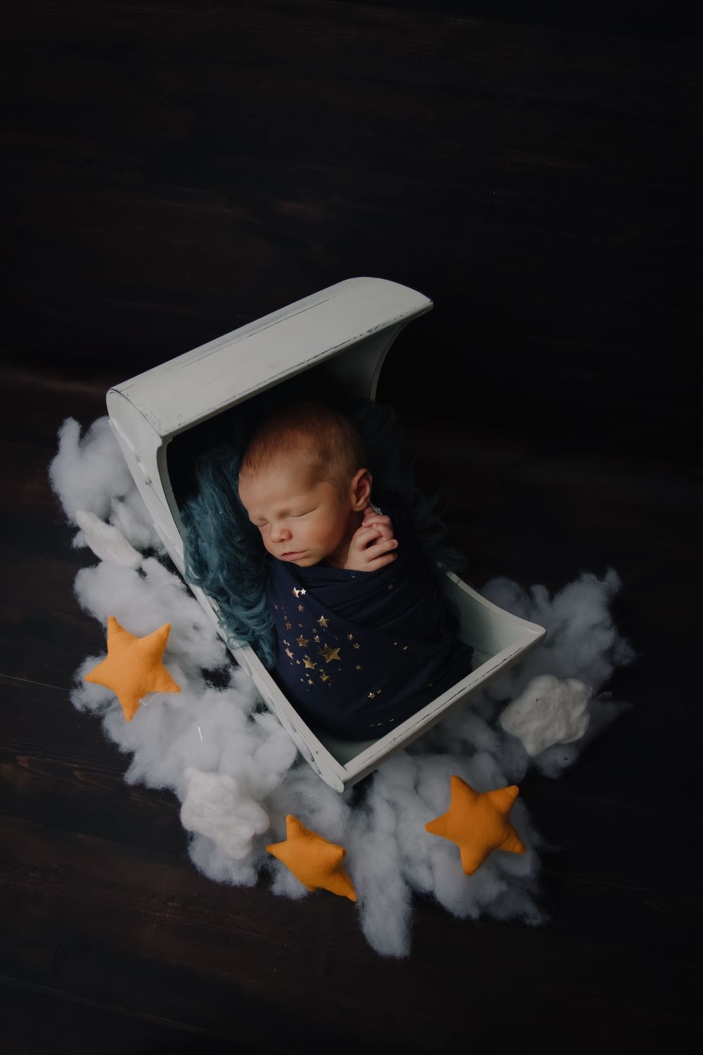Dreamy newborn photo with stars and clouds in white frame against dark background.