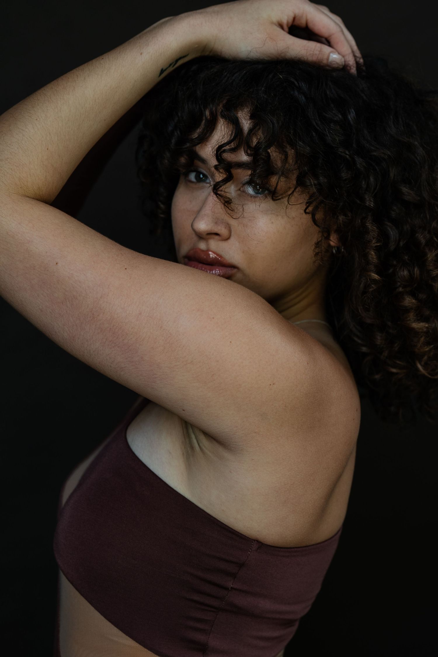 Artistic portrait with curly hair and burgundy top against dark background.