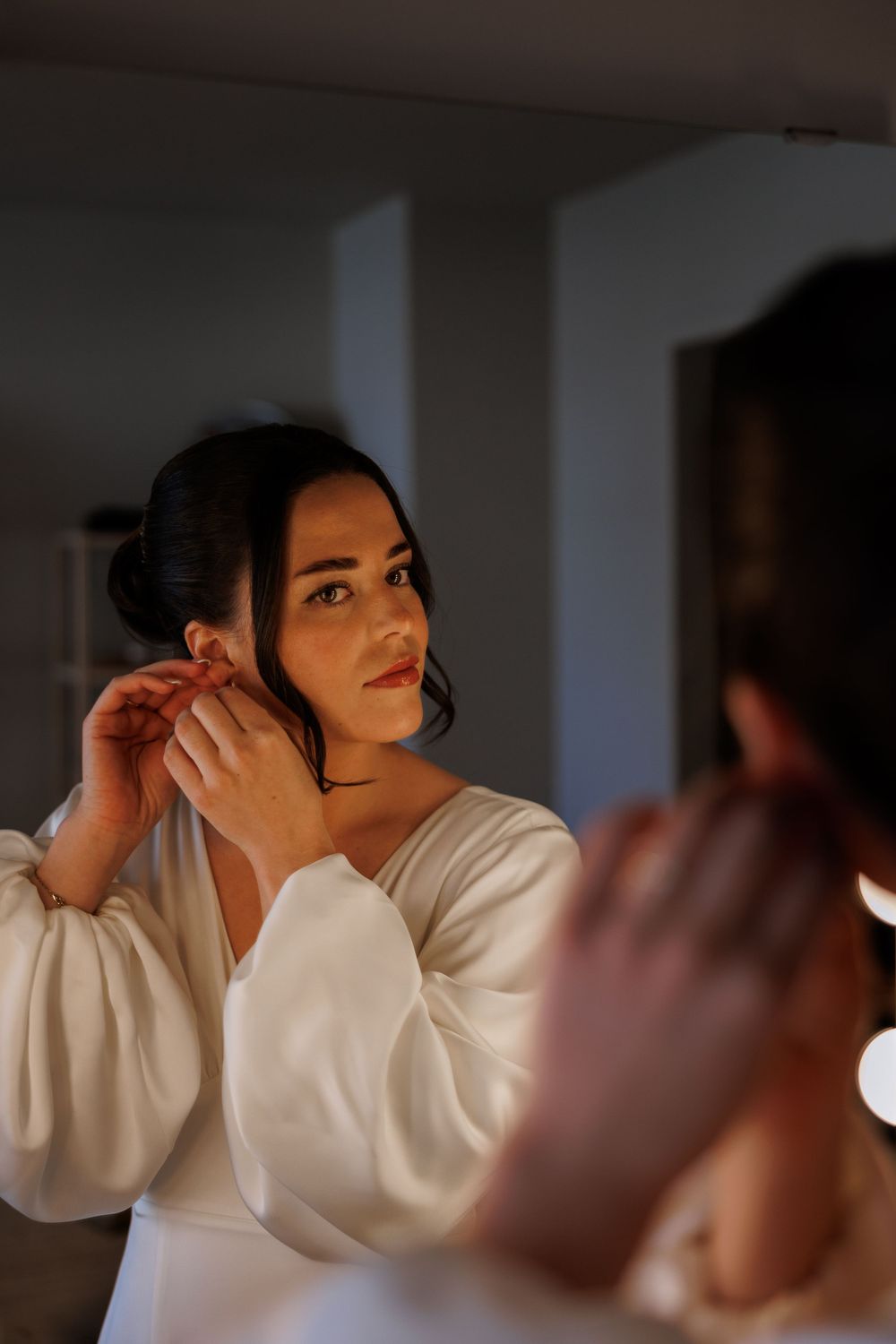 A bride in an elegant white dress adjusts her earring while getting ready.