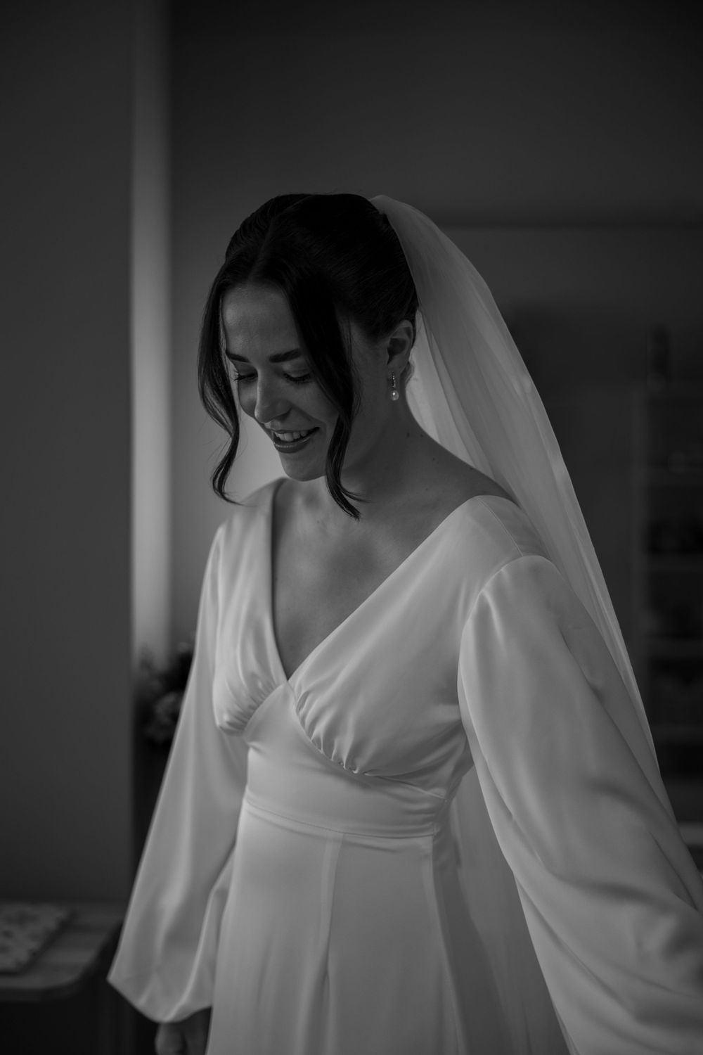 A candid black and white portrait of a bride in a flowing white dress with balloon sleeves.
