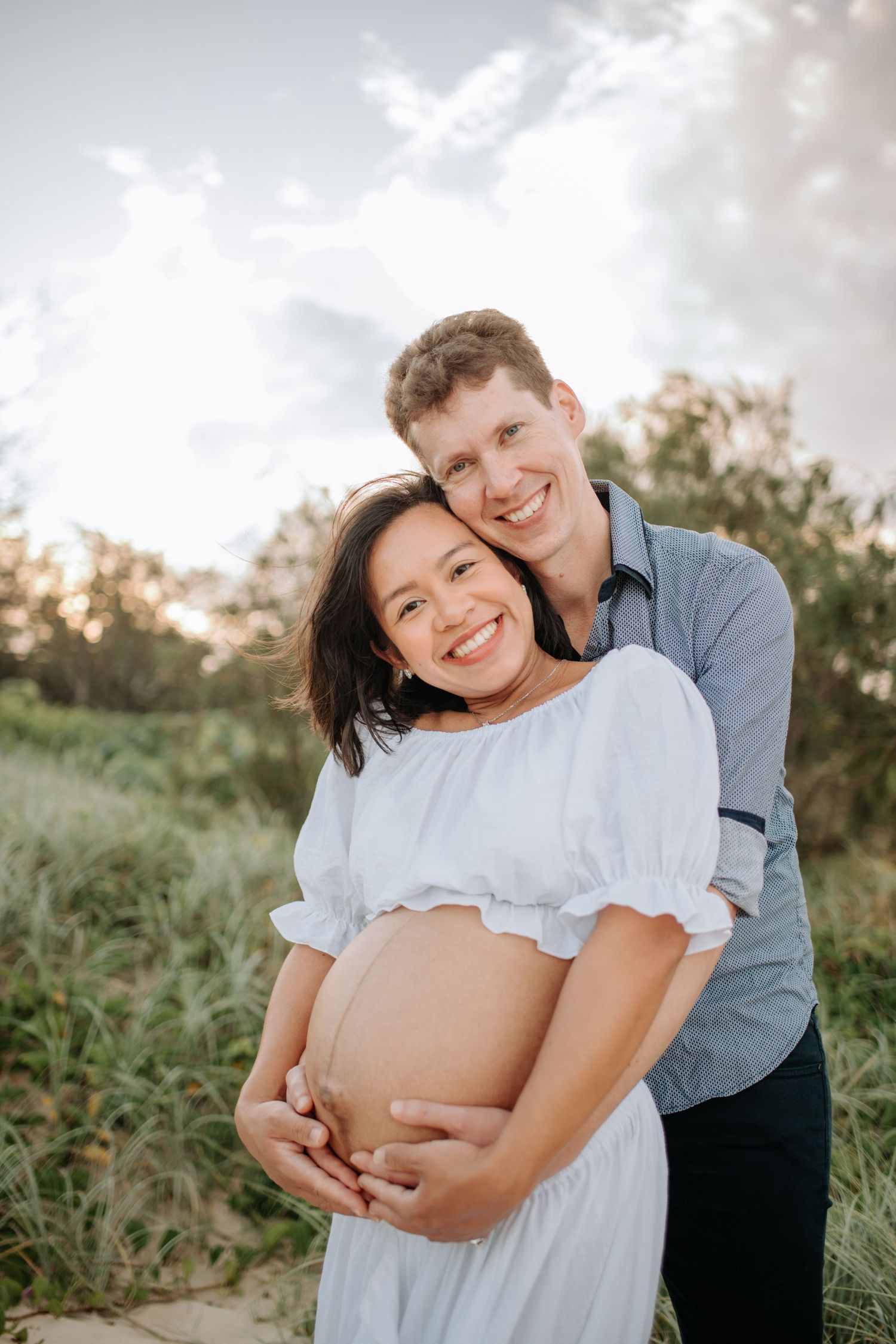 Joyful maternity portrait of couple embracing outdoors in natural setting.