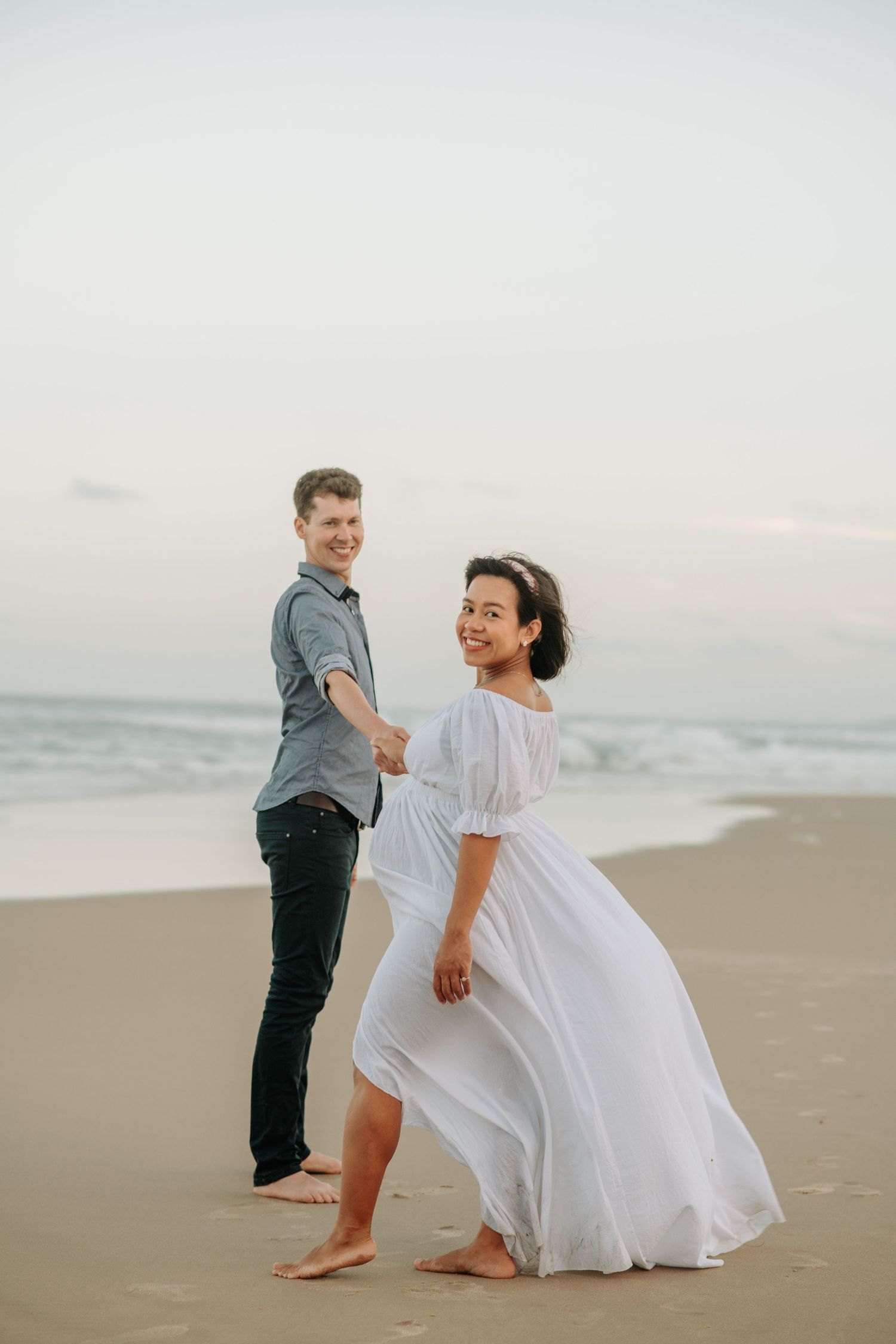 Couple enjoying romantic moment on beach during maternity photoshoot.