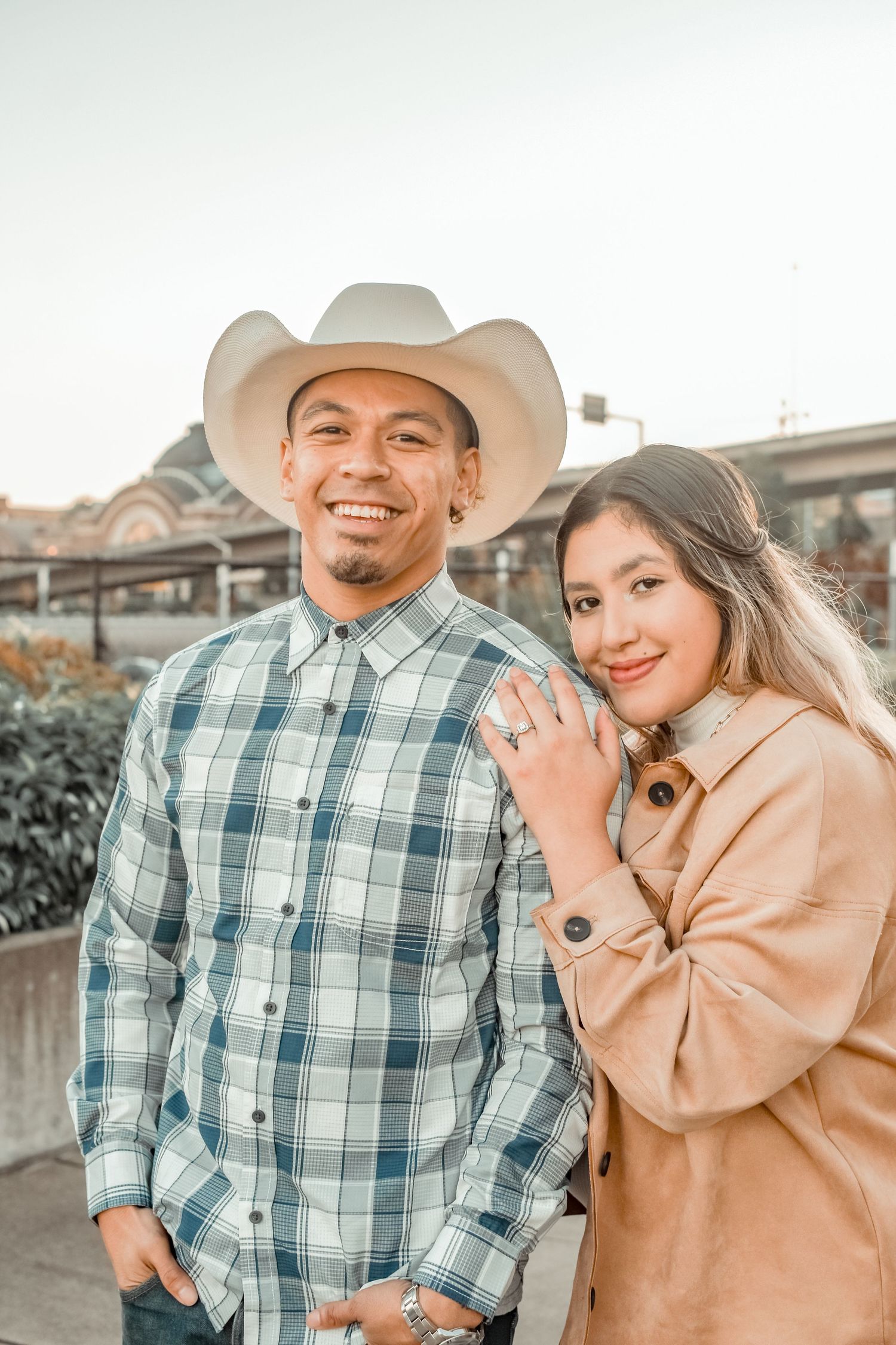 Couple in casual western wear showing off engagement ring outdoors.