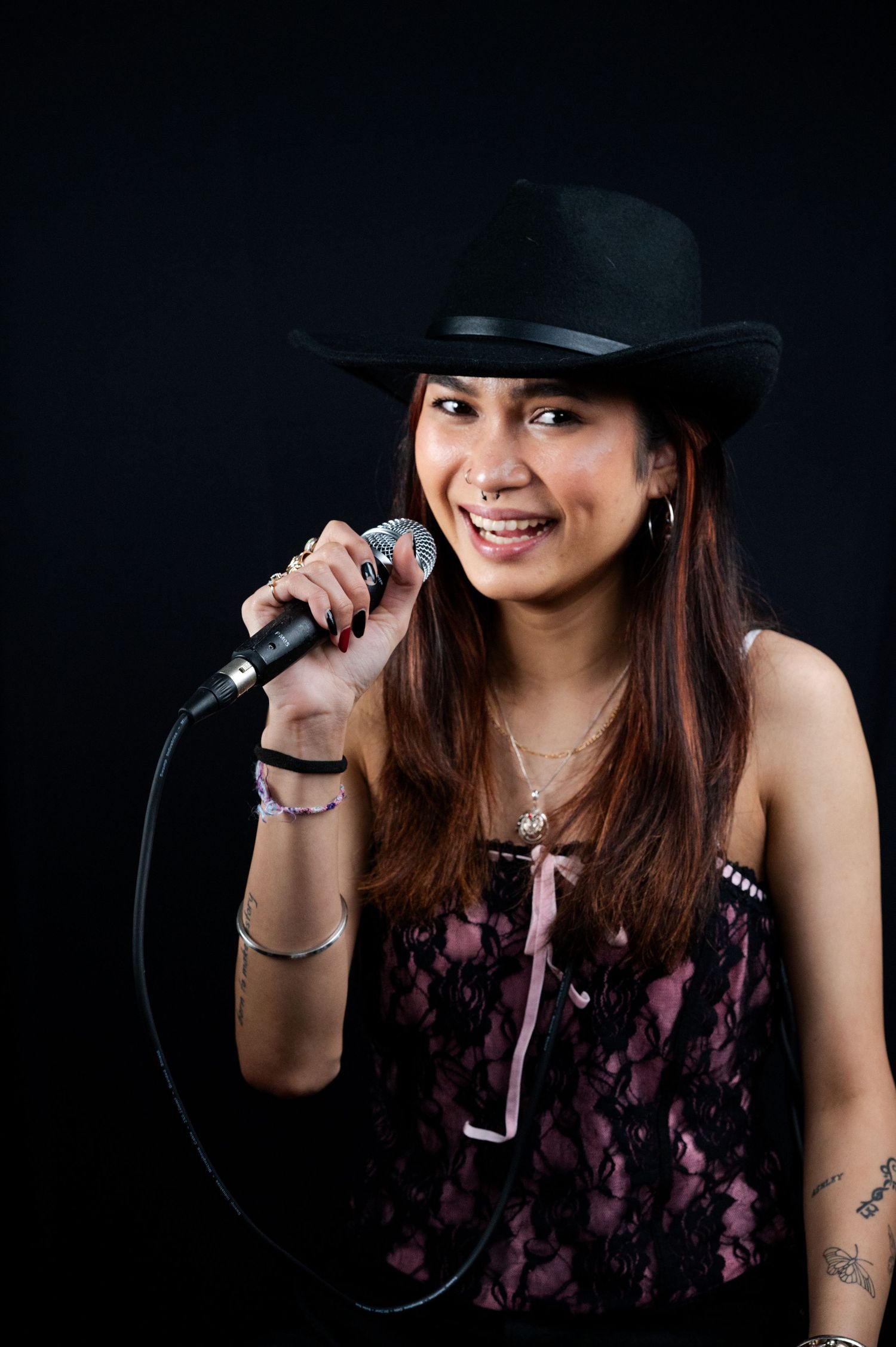 Young woman singer in a black cowboy hat holding a microphone on a dark stage.