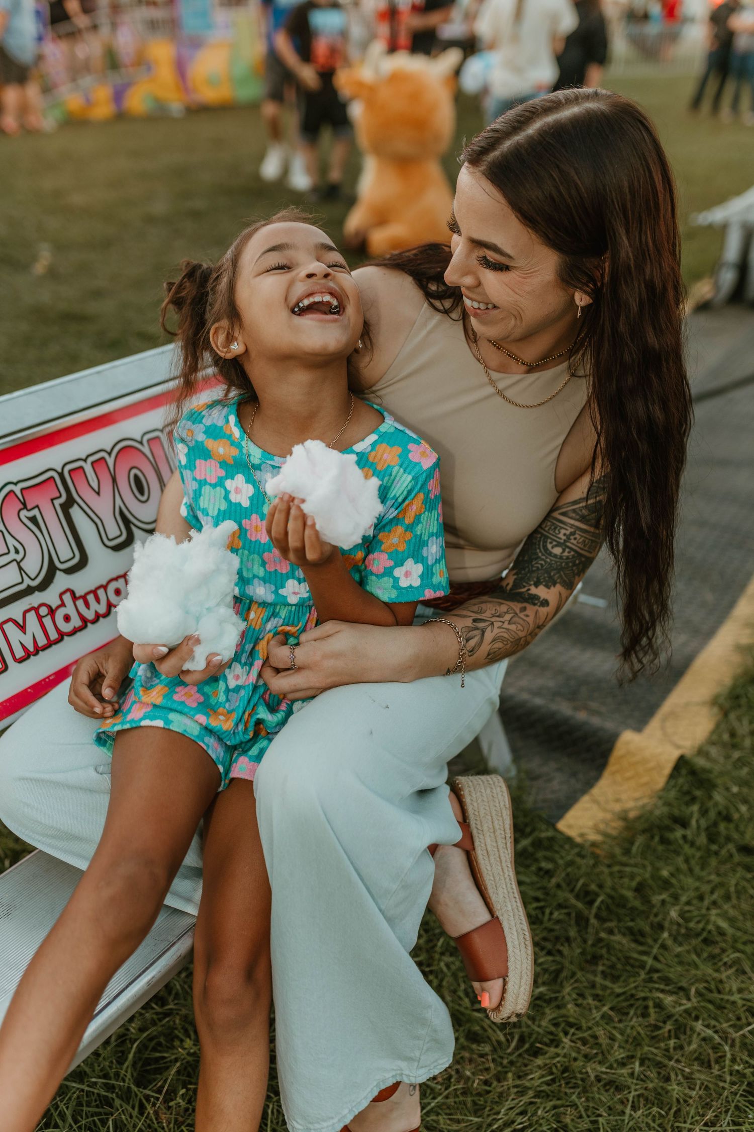 Two people share a joyful moment while enjoying cotton candy at an outdoor carnival.