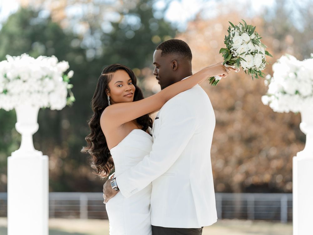 A romantic wedding couple shares an intimate kiss during their outdoor ceremony with white floral decorations.