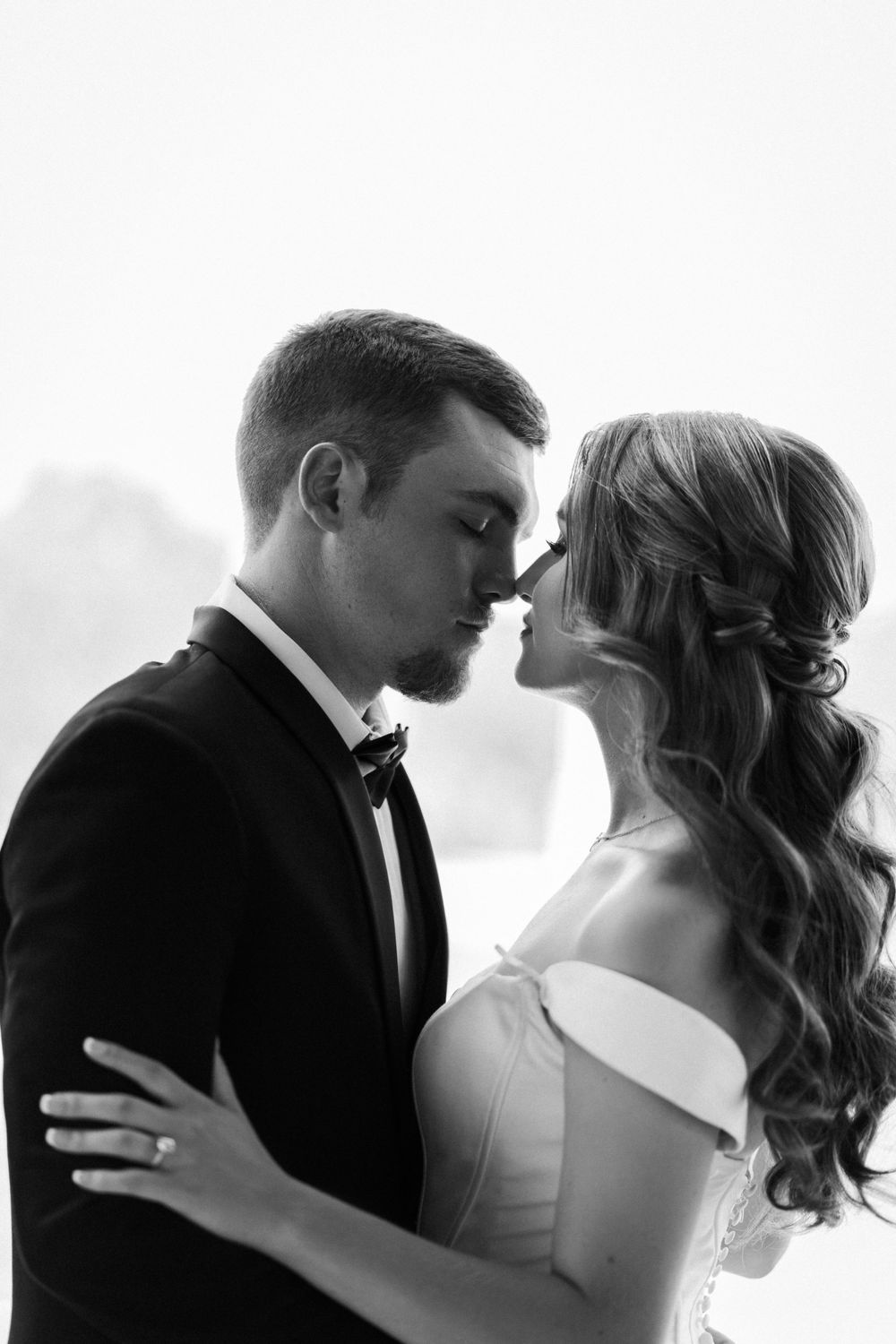 Black and white romantic portrait of a couple in wedding attire about to kiss.