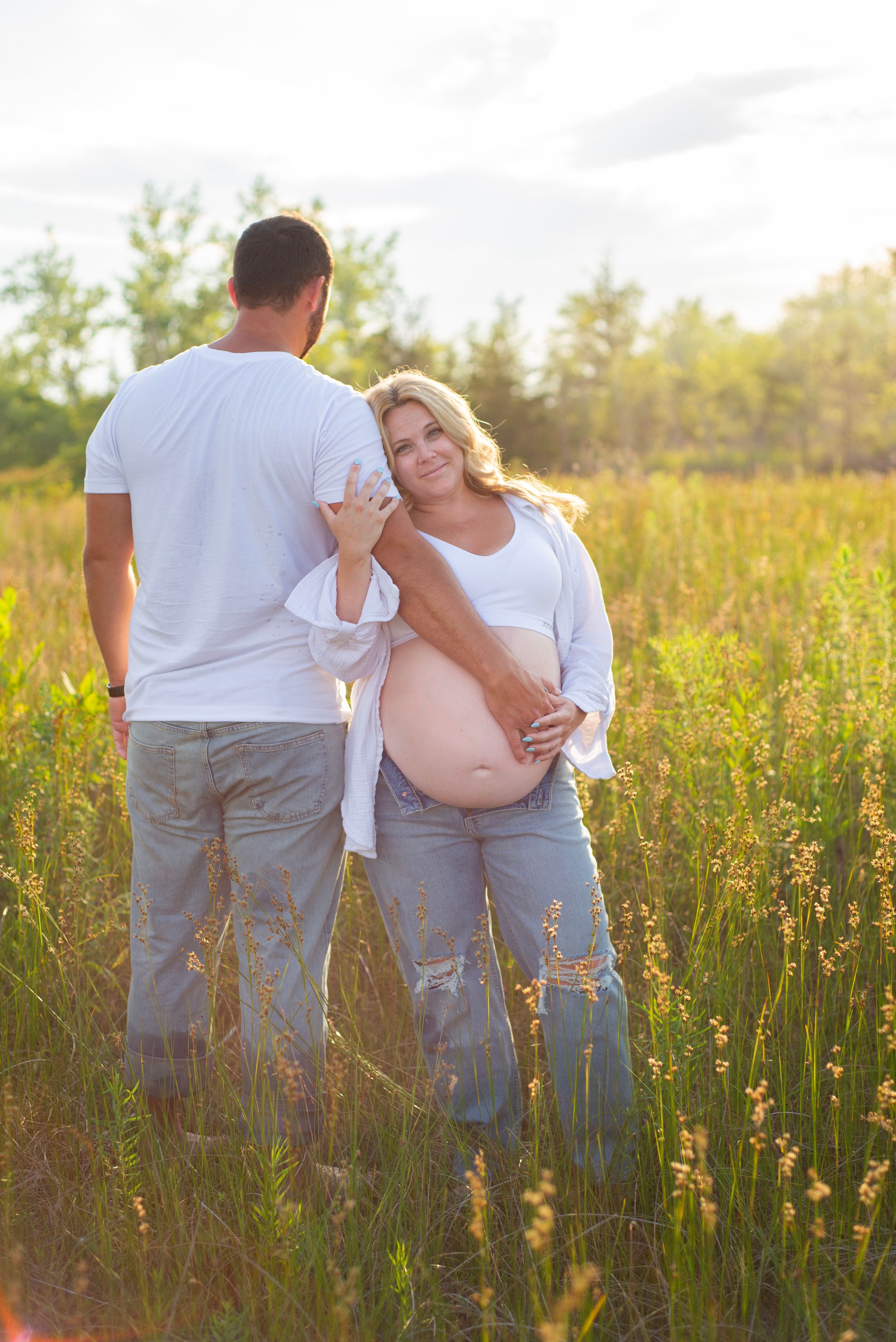 A couple poses in a sunlit meadow during a maternity photo session.