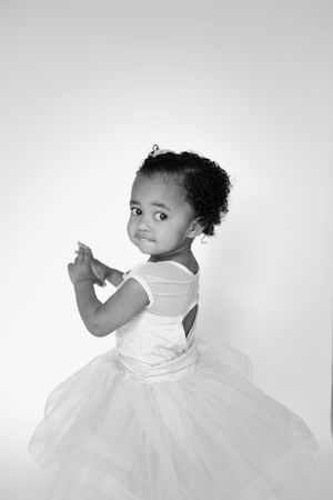 Artistic black and white photos of a young child in a white dress twirling against a light background.