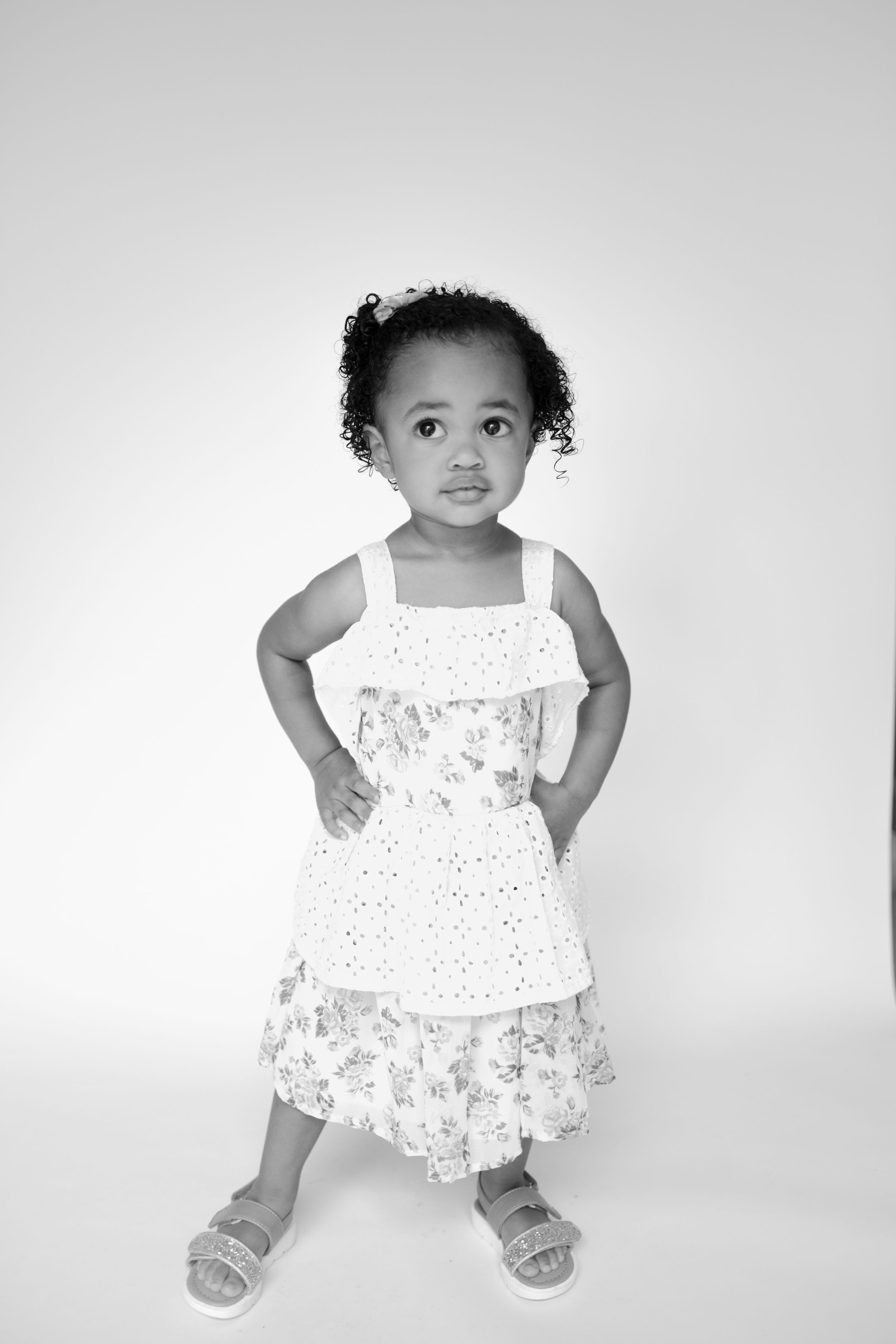 Child wearing a white lace dress poses in different playful positions against a light background.