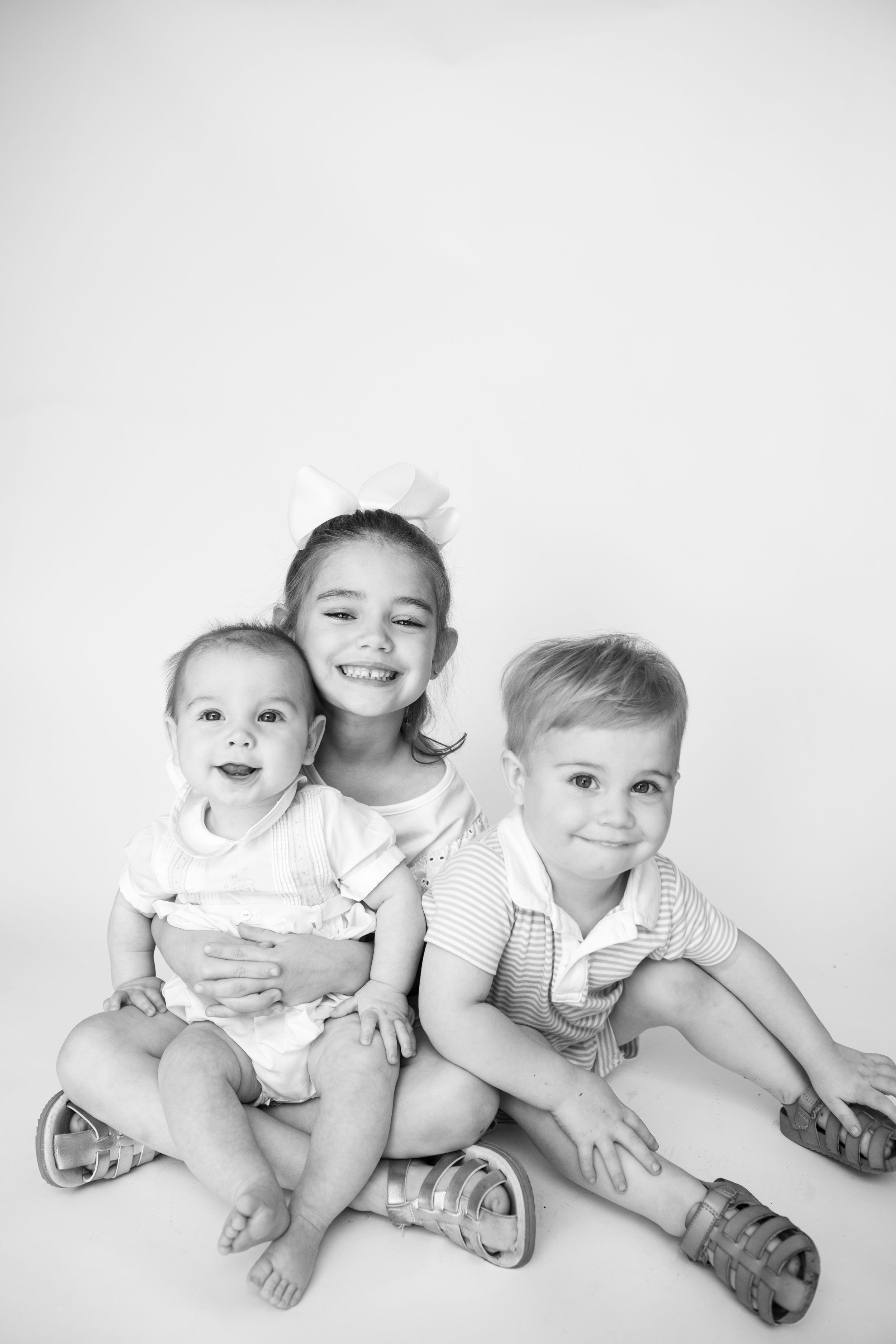 Black and white portrait of three children laying together playfully on a white background.