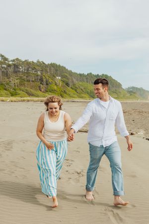 Playful couple running and splashing along sandy beach shoreline.