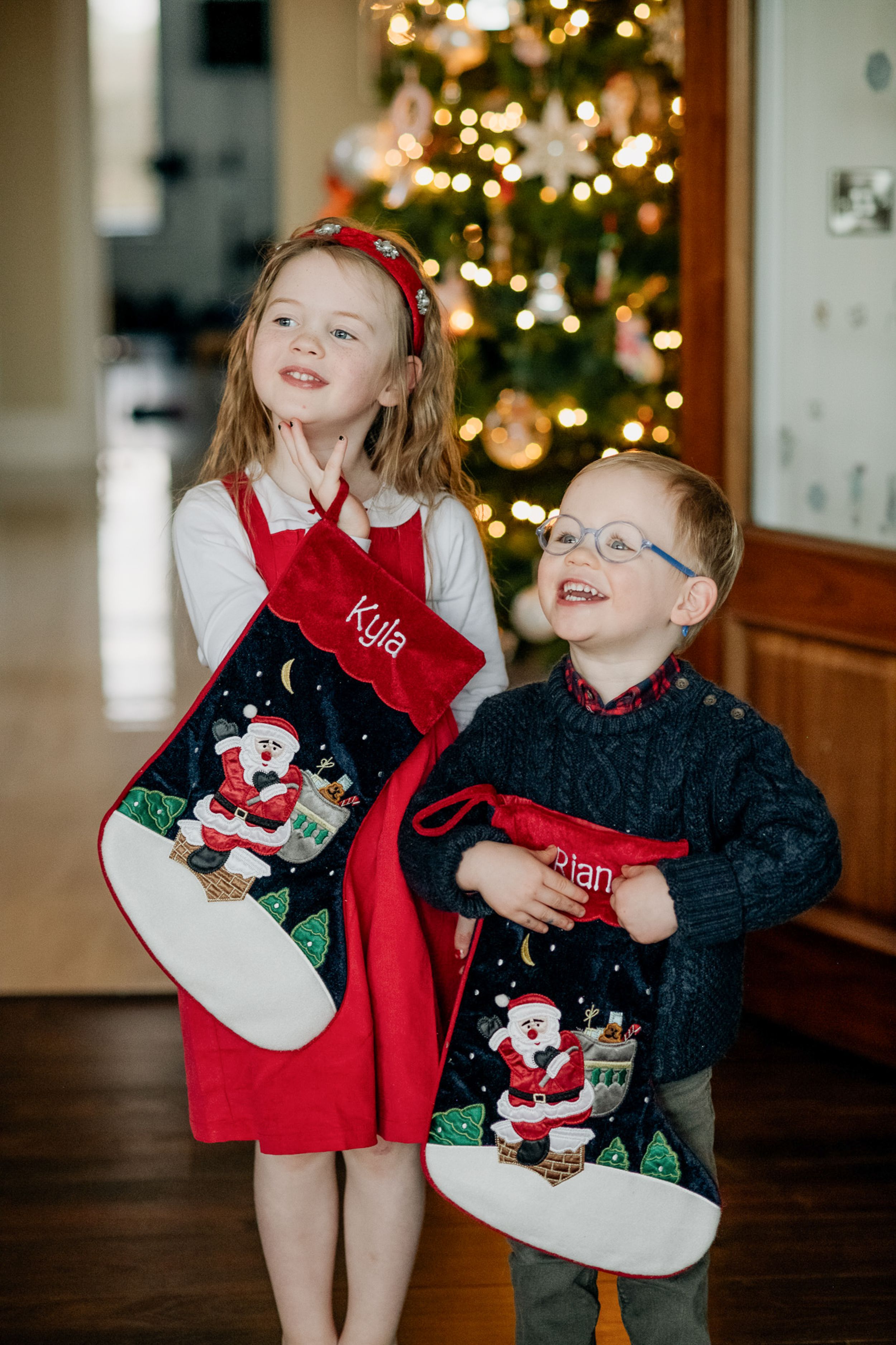 Children in festive clothing decorating a beautifully adorned Christmas tree in a cozy, well-lit living room.