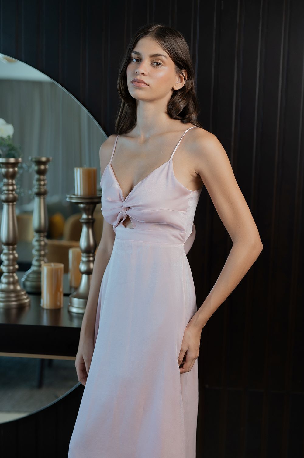 Light pink satin evening dress with spaghetti straps and front tie detail in an elegant interior setting.