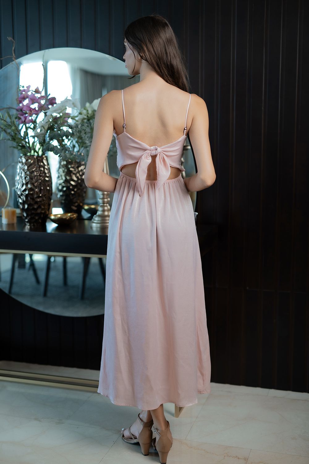 Back view of a pink midi dress featuring a bow detail and spaghetti straps, shown in an elegant setting.