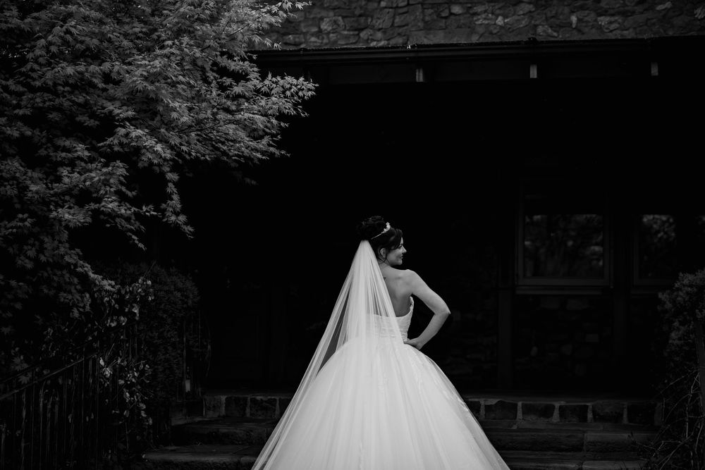 Black and white photo of a bride in a full ballgown wedding dress standing in a garden setting.