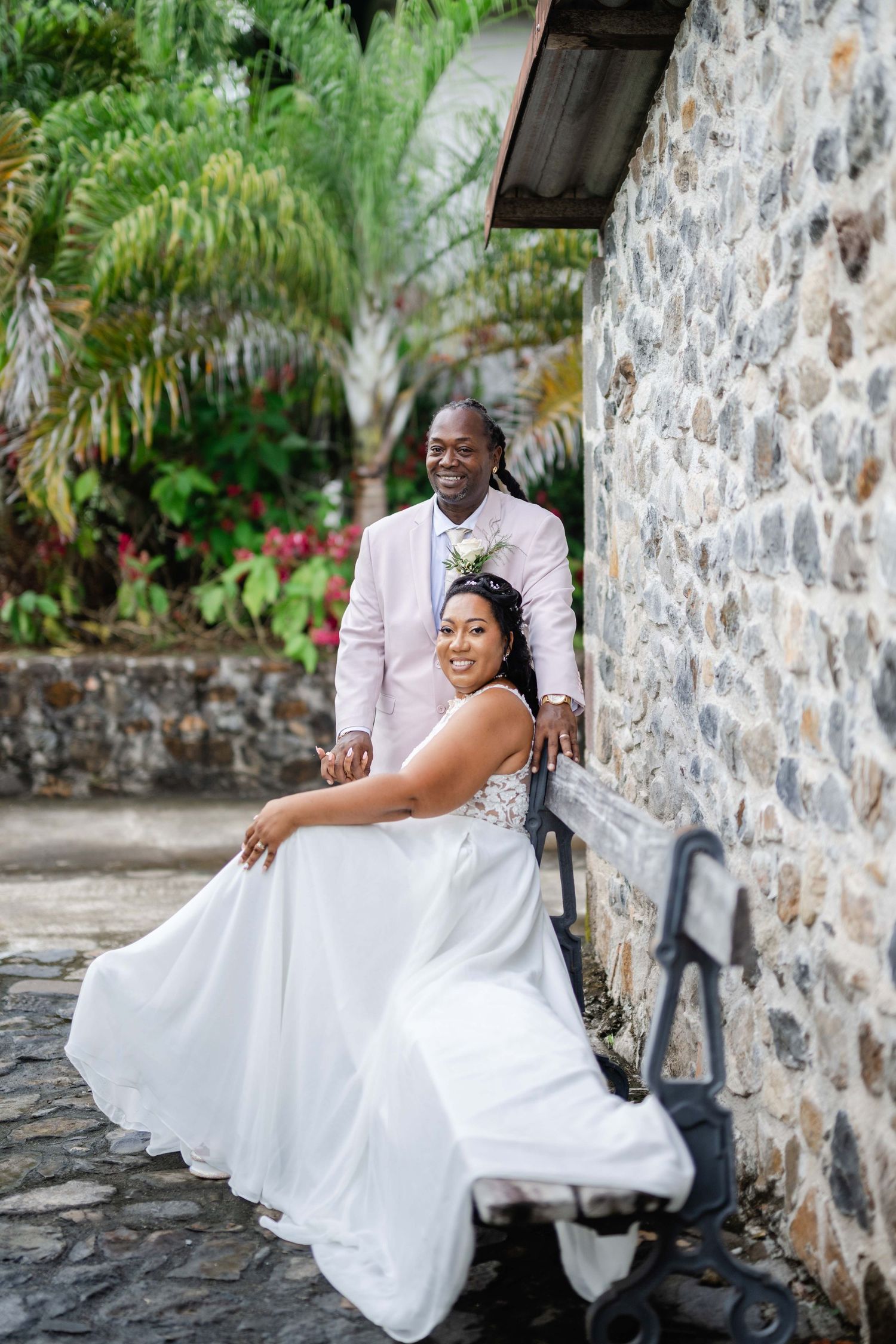 Couple de mariés à l'habitation La Salle à Sainte marie en Martinique.La mariée est assise sur un banc avec le marié debout derrière elle.