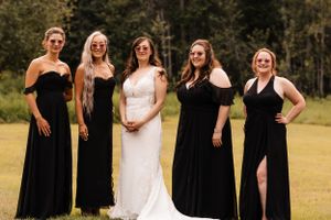Bride in white gown poses with four bridesmaids in black dresses outdoors.