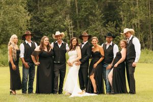 Wedding party in black attire and cowboy hats poses together on a green lawn.